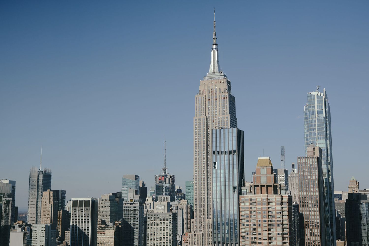 New York City skyline with iconic Empire State Building towering among modern skyscrapers against a blue sky.