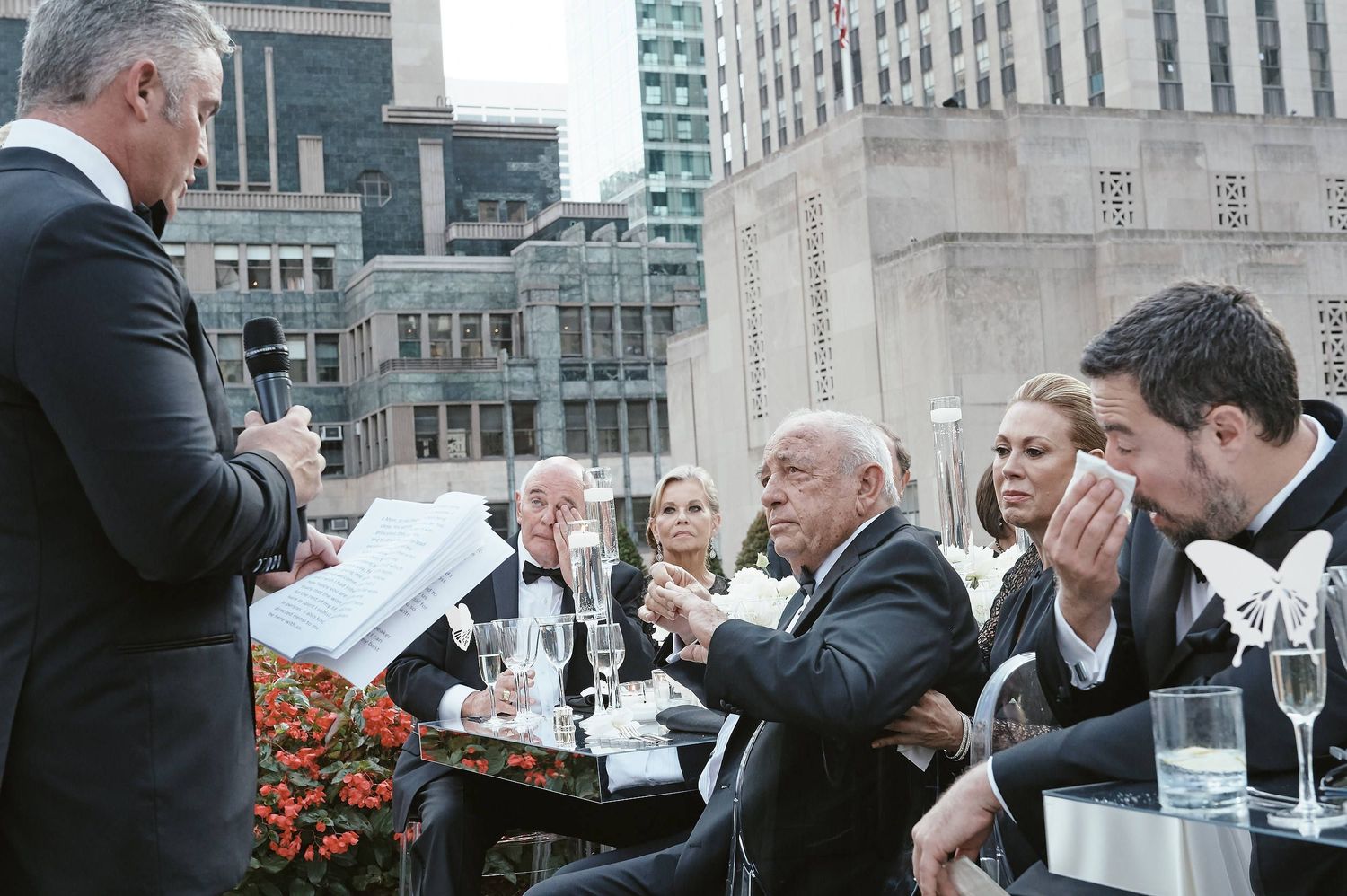 A group of people enjoying drinks and conversation on an outdoor rooftop patio with city buildings in the background.