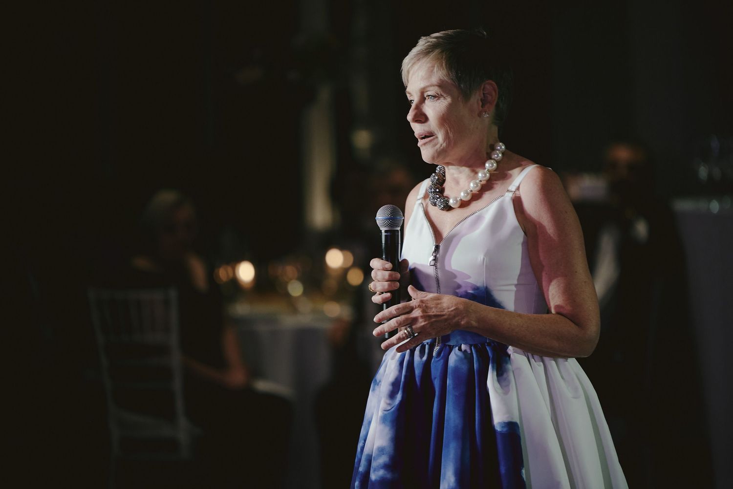 A person in a blue and white dress holding a microphone during an evening reception.