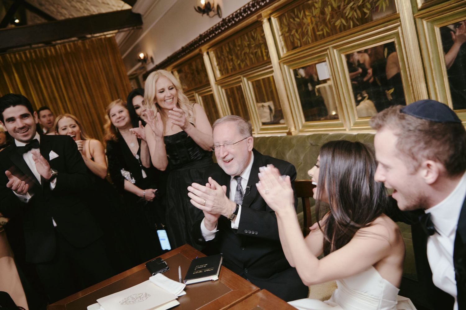 Wedding guests and newlyweds sharing joyful laughter and reactions at an elegant venue with wood paneled walls.