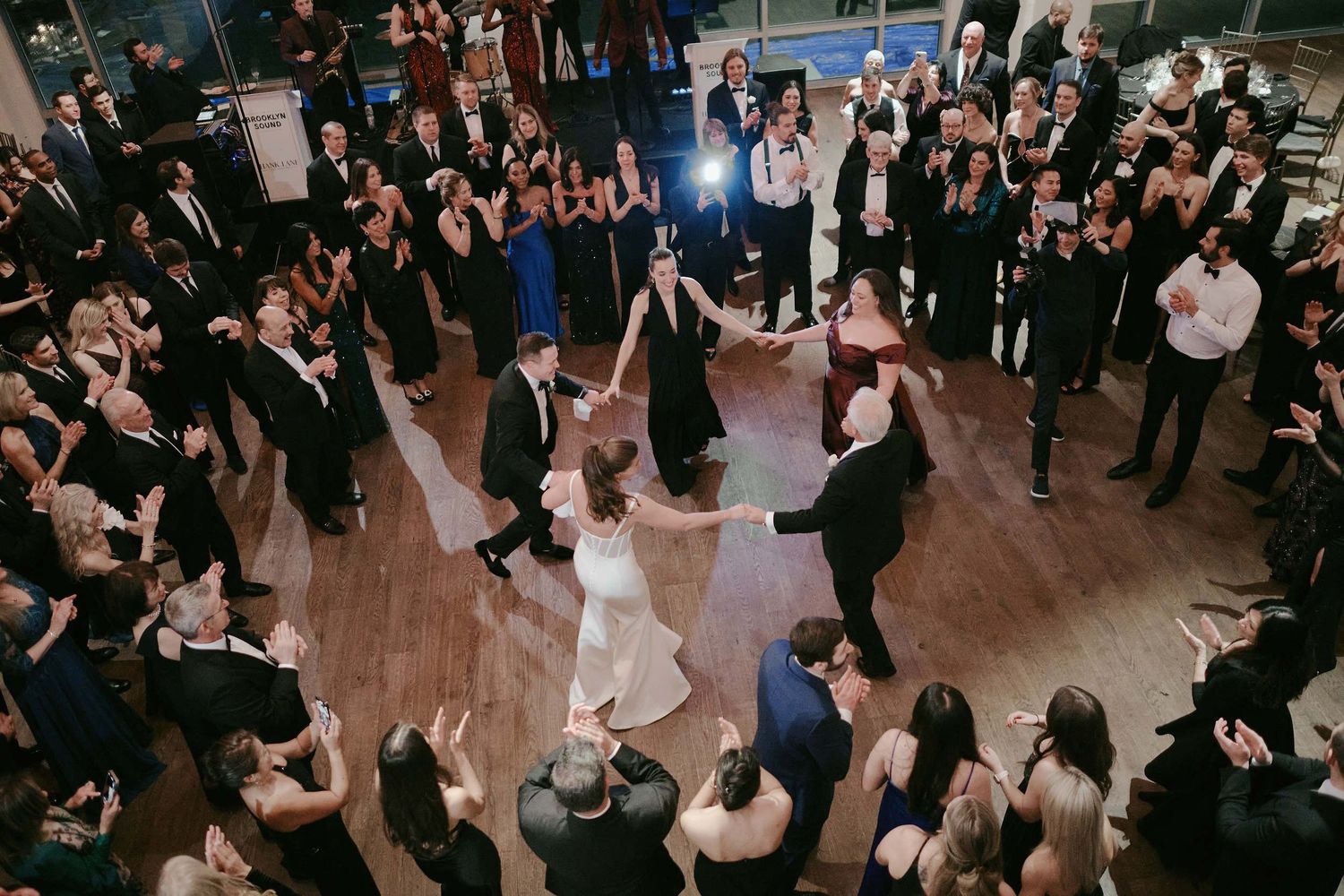 Guests gather in a circle on a wooden dance floor at an elegant reception while celebrating a special occasion.