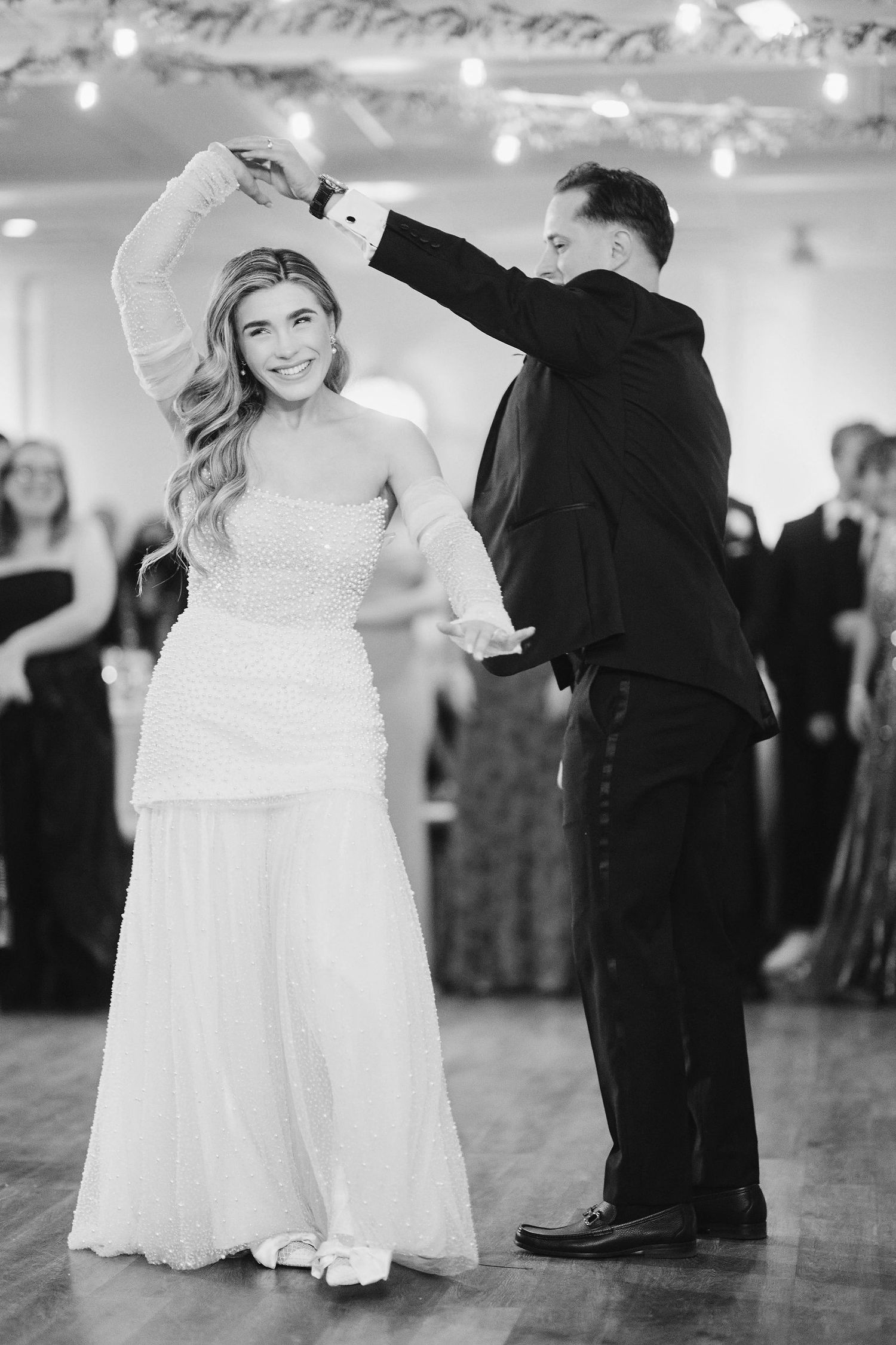 A couple performs their first dance at a wedding reception, with the bride in a white dress and the groom in a black suit.