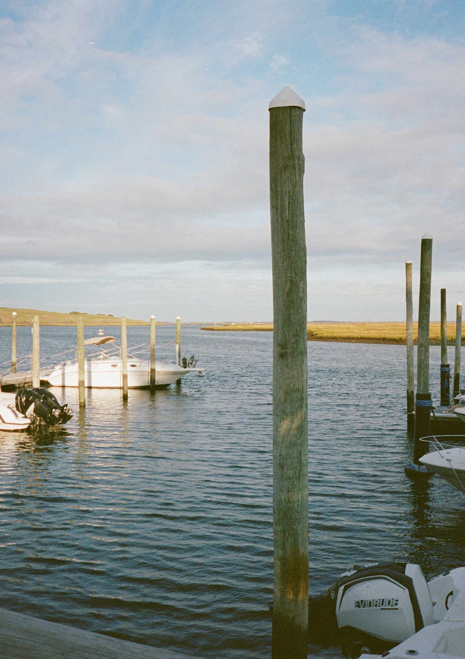 Wooden dock pilings rise from calm waters with boats moored alongside them on a peaceful coastal waterway.