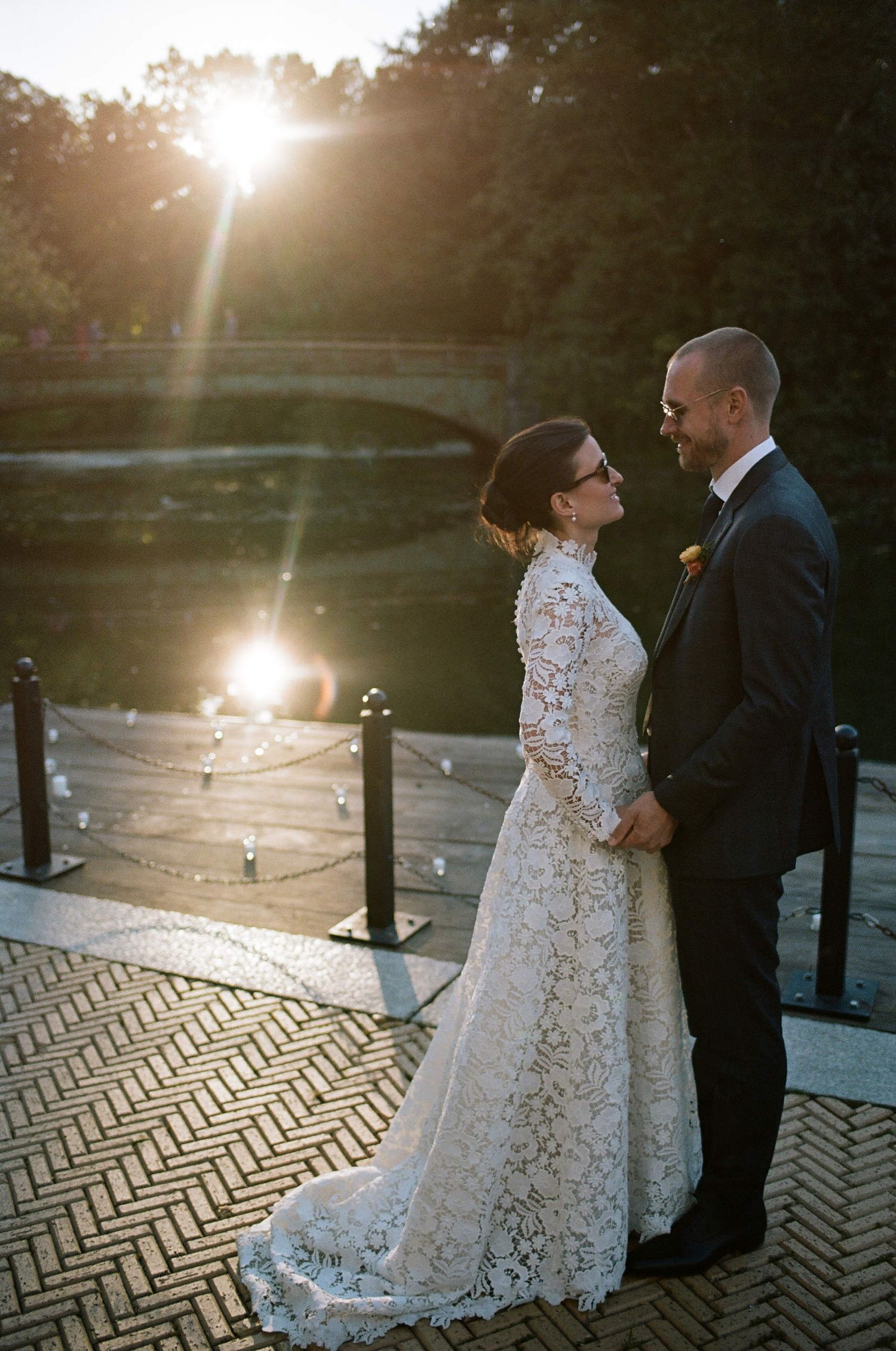 Newlywed couple shares romantic moment at sunset on wooden deck by water with beautiful lensflare effect.