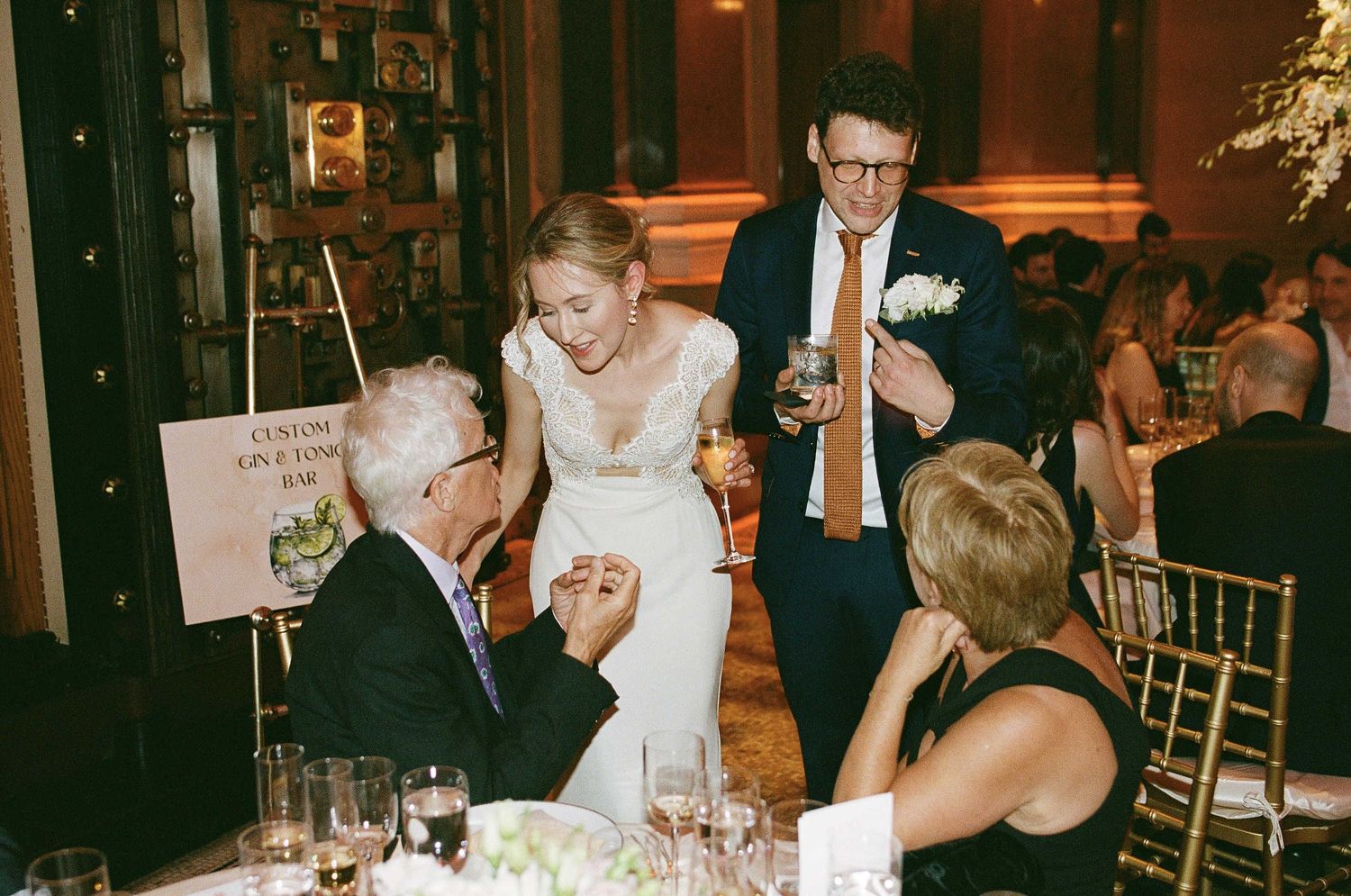 Wedding couple and guests share an intimate moment at their reception table in a warmly lit venue.