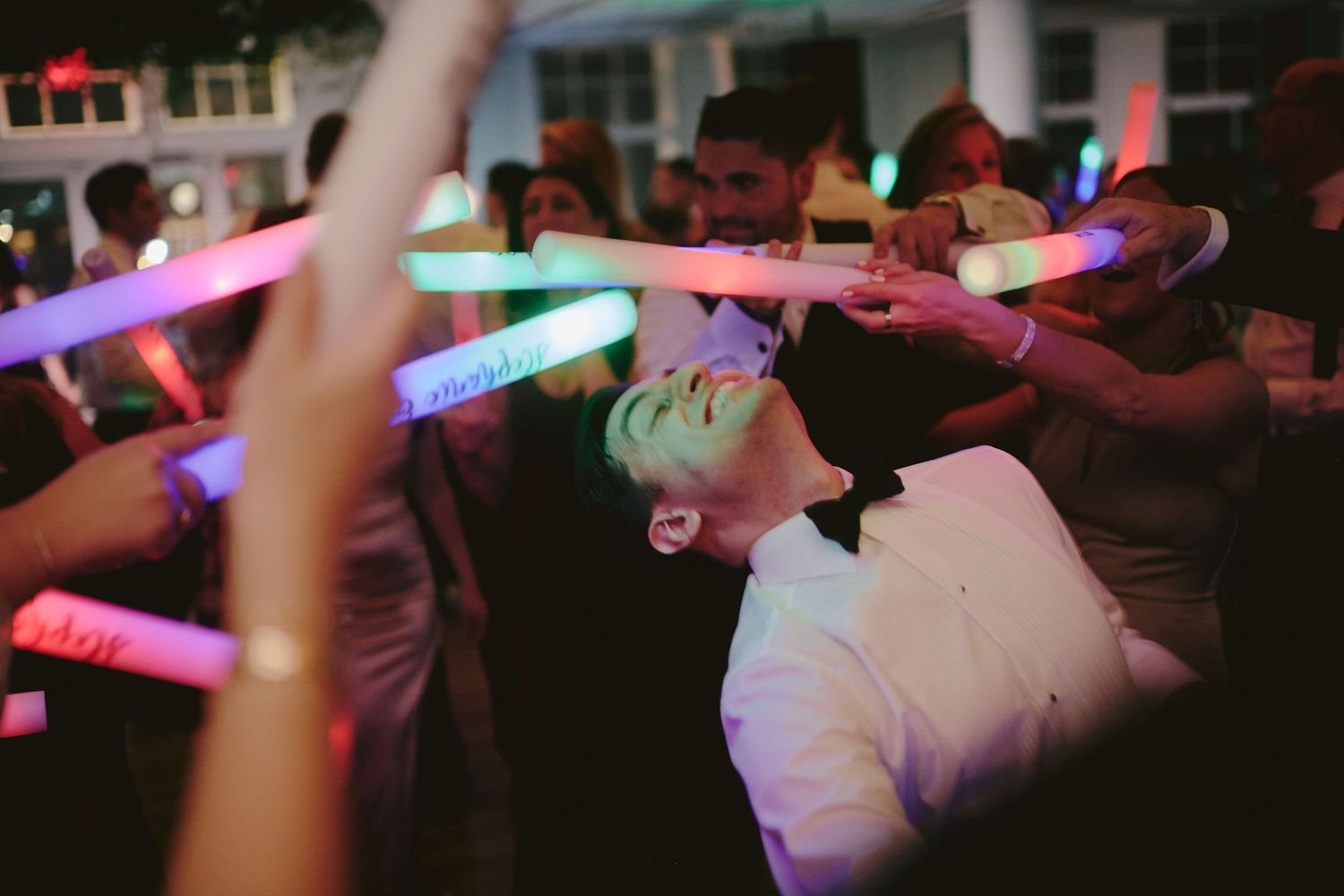 Party crowd dancing under colorful glow sticks and LED lights at a nighttime celebration.