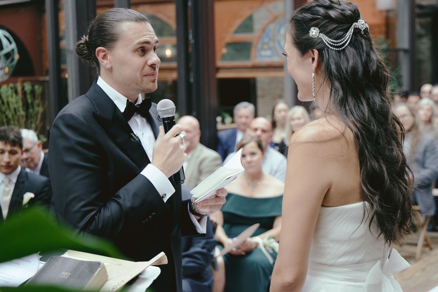 A couple exchanges vows at their outdoor wedding ceremony while guests look on in the background.