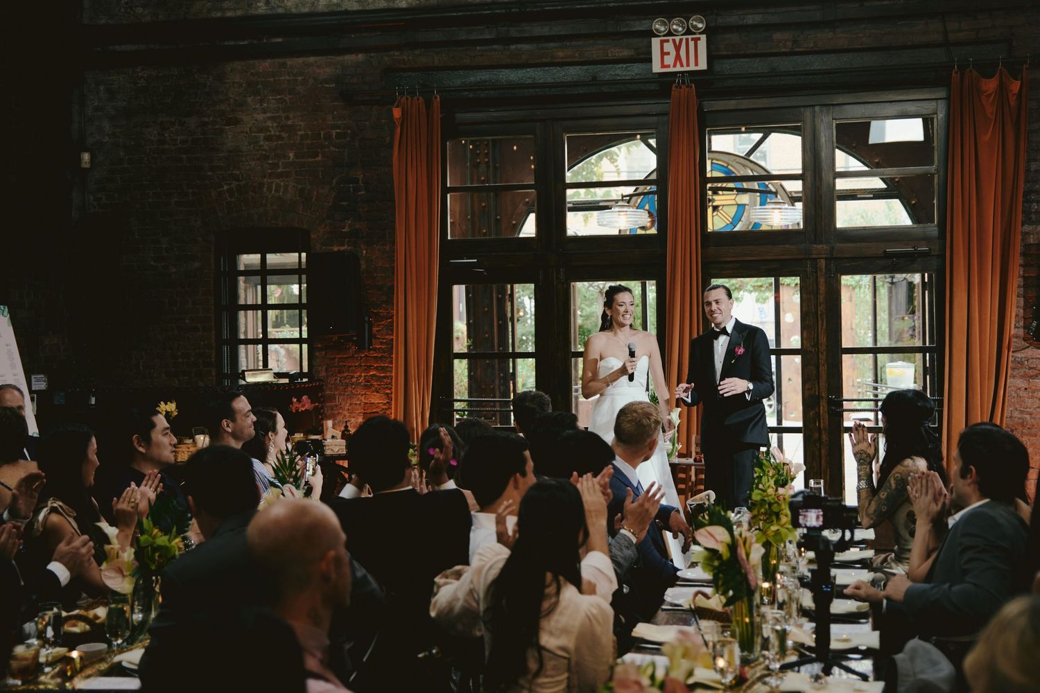 Wedding guests gathered in a rustic restaurant venue with wooden panels and large windows during a reception celebration.
