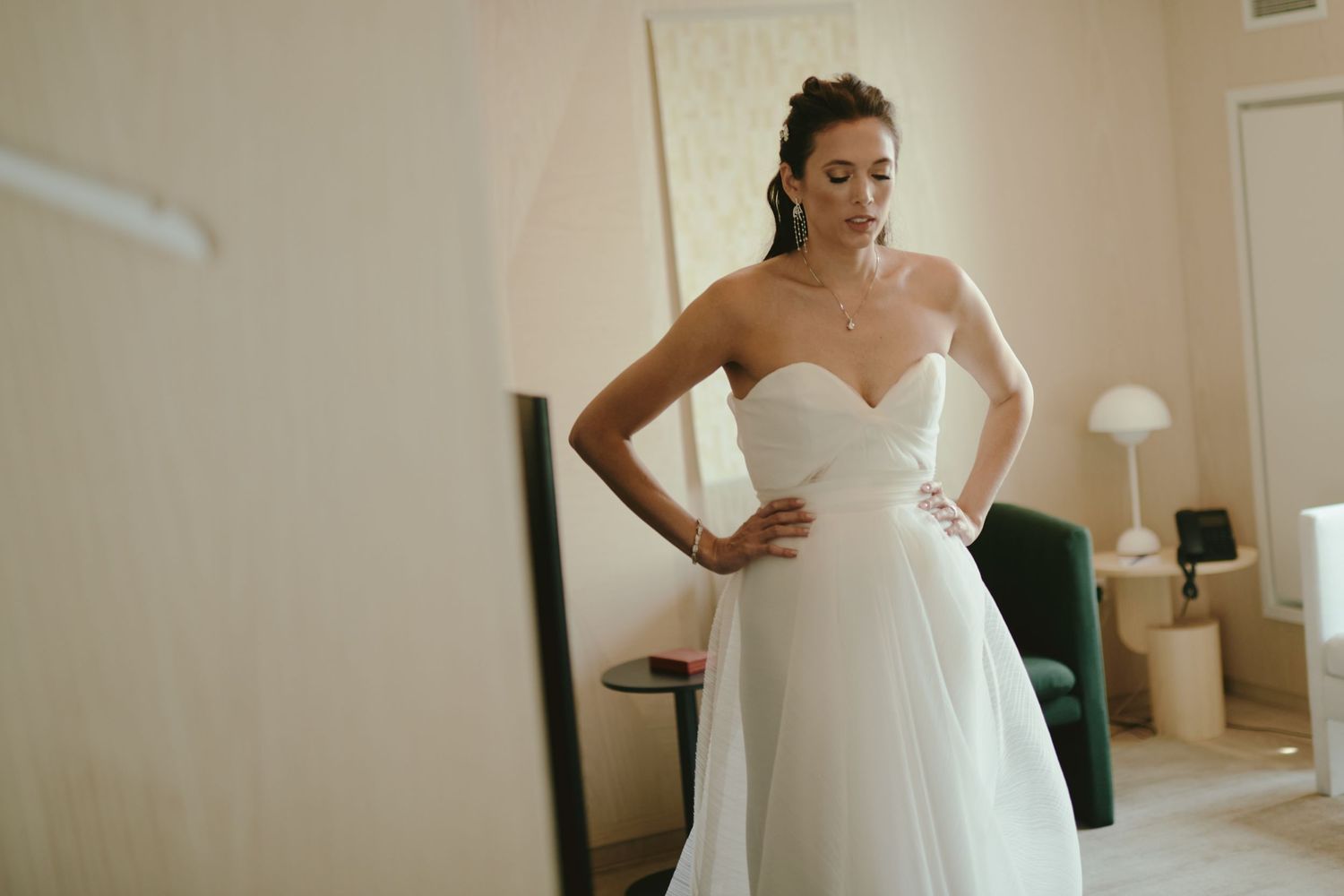 A strapless white wedding gown with a flowing tulle skirt is shown in a softly lit room with neutral decor.