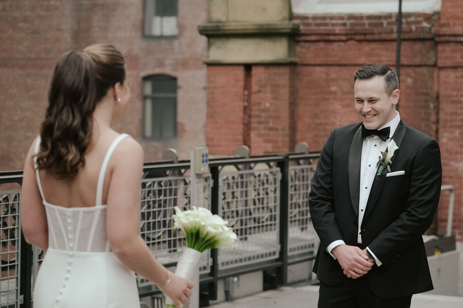 A first look moment between newlyweds on an urban balcony with brick architecture backdrop.