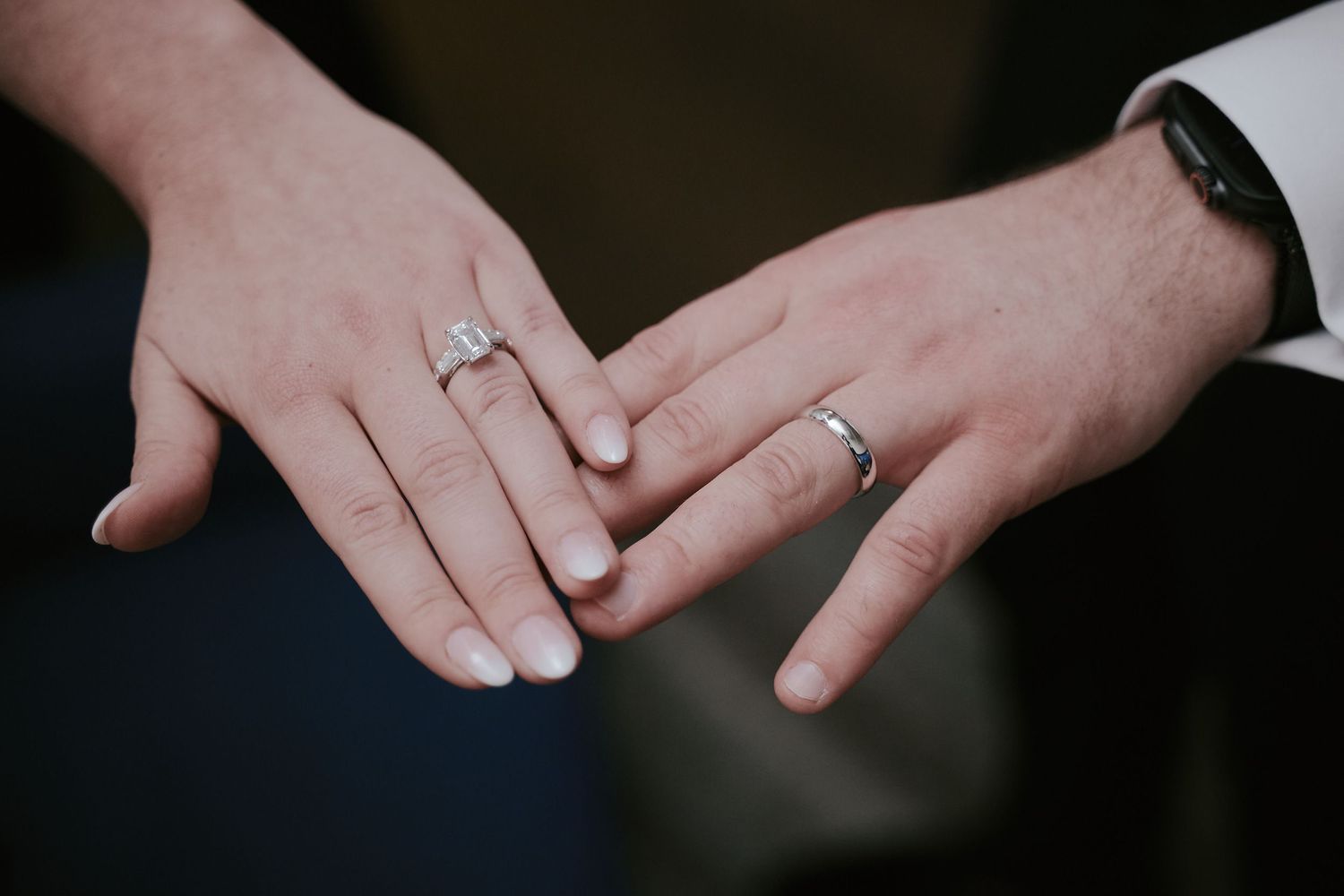Two hands with wedding rings gently touch against a dark background showing love and commitment.