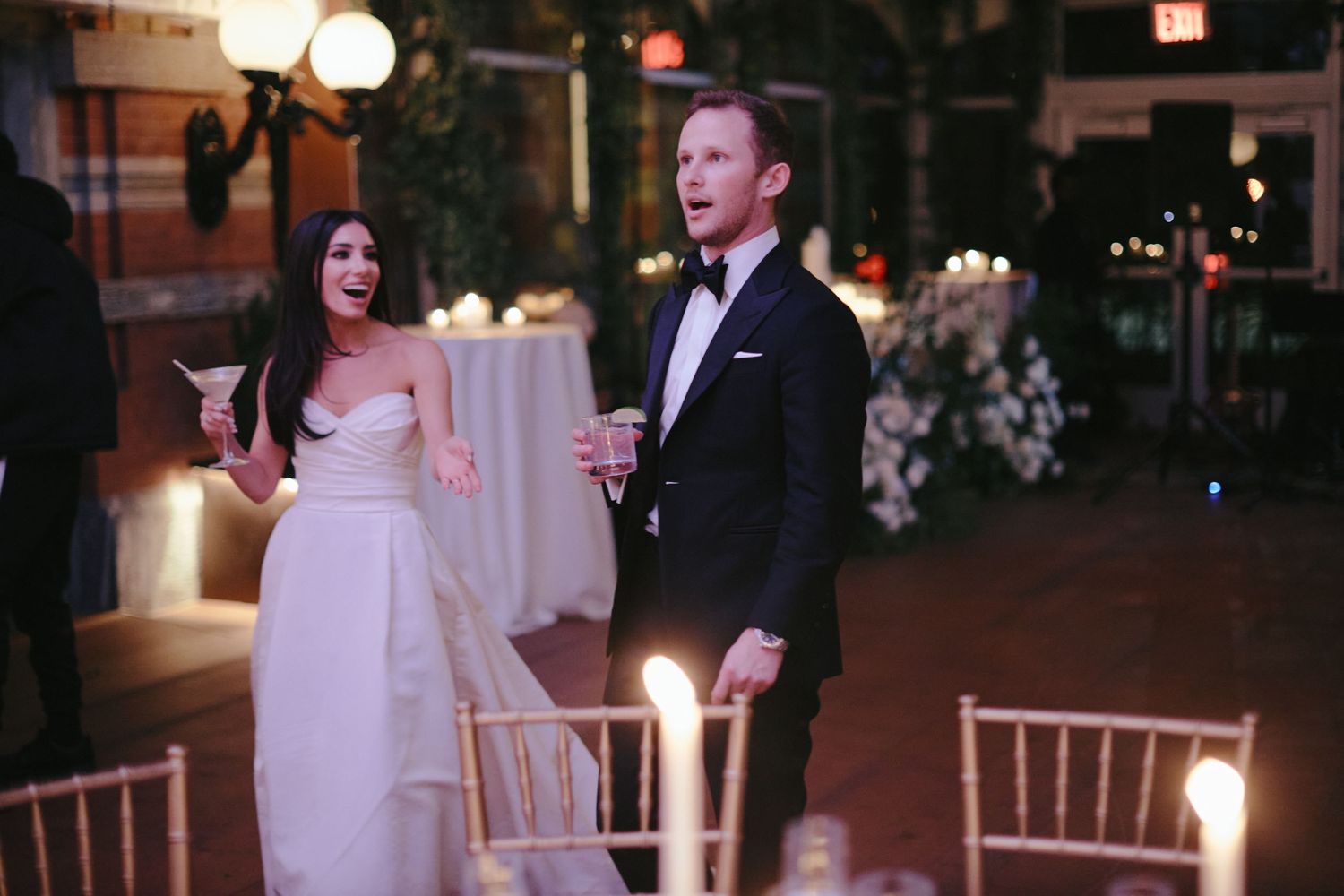 A couple shares an intimate moment at an elegant candlelit wedding reception with decorative lighting and floral arrangements.