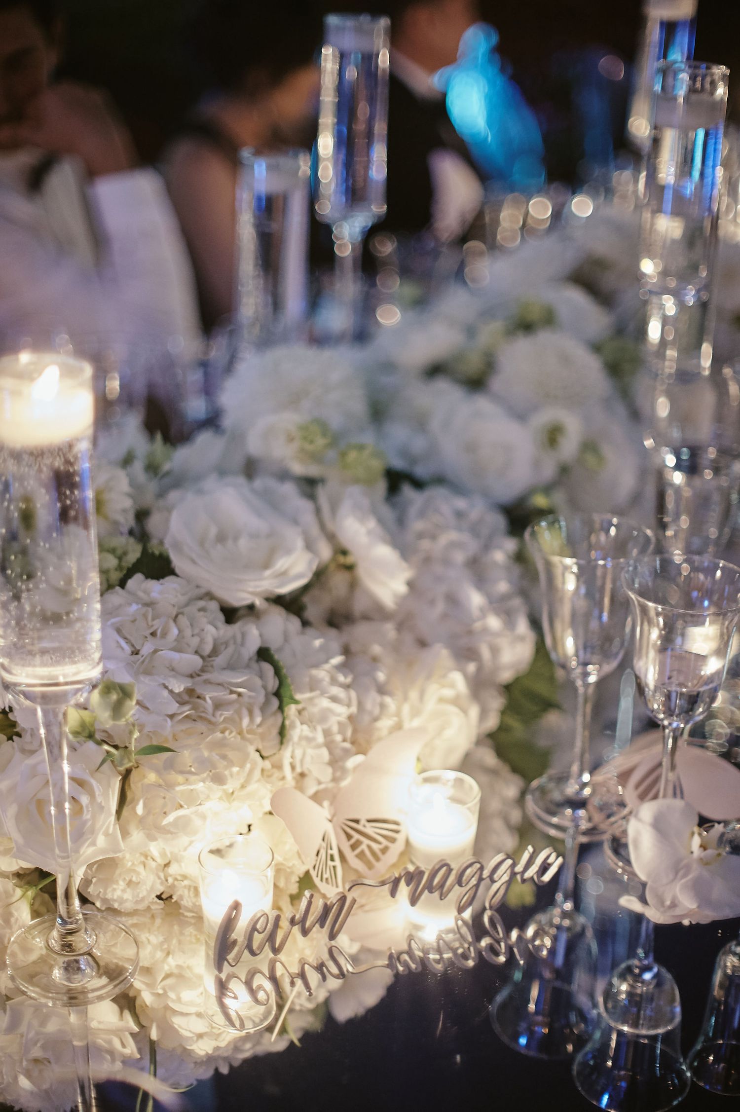 Luxurious wedding table setting with white roses, crystal glassware, and glowing candles at an evening reception.