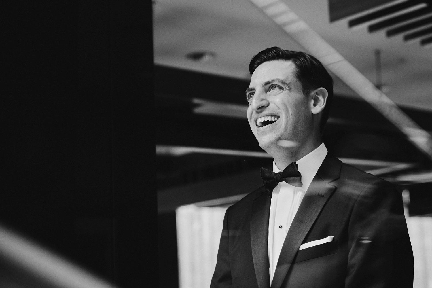 Black and white photograph of a smiling person in a formal tuxedo and bow tie during an elegant event.