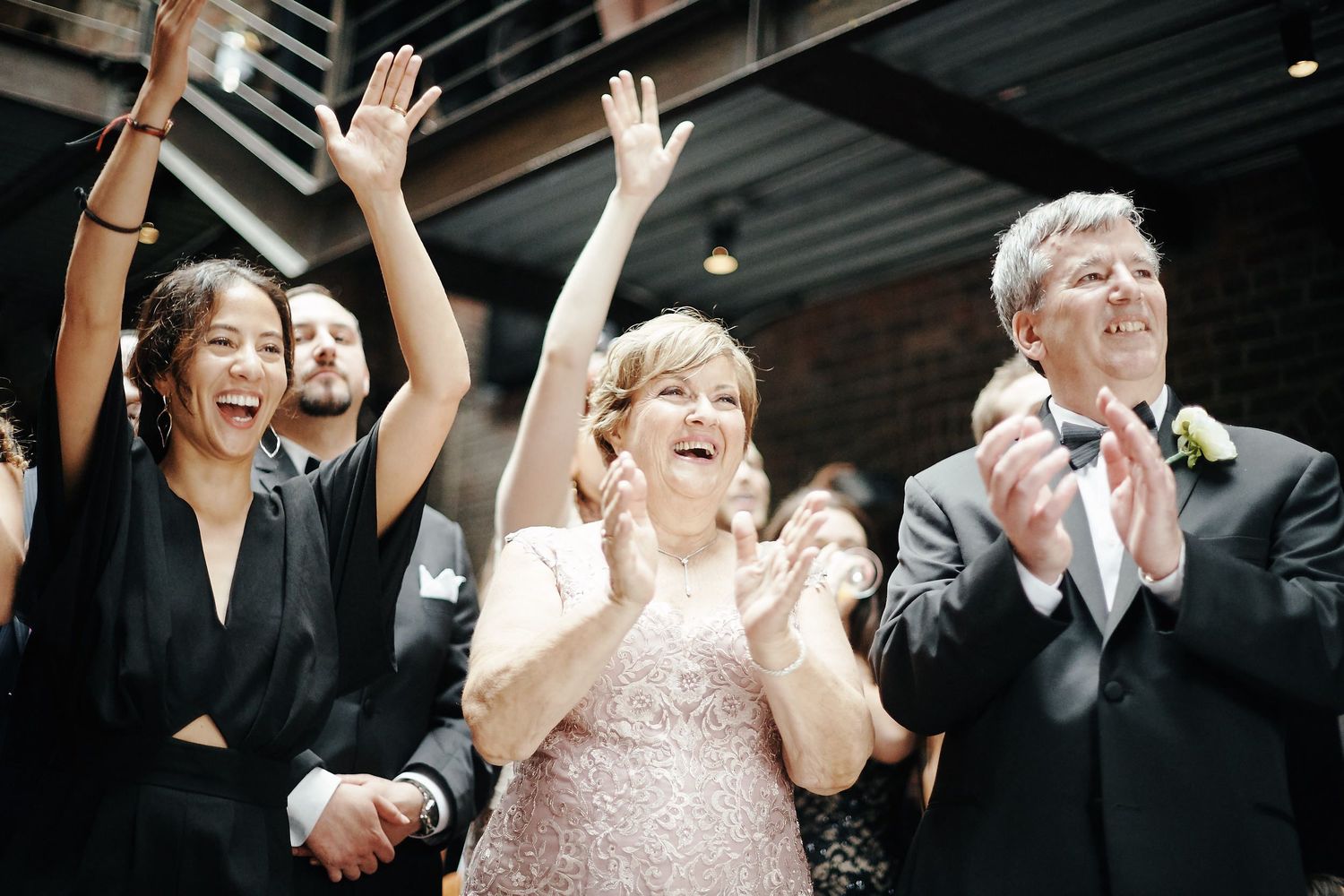 A group wearing formal attire celebrates with raised hands and joyful expressions at an elegant indoor event.