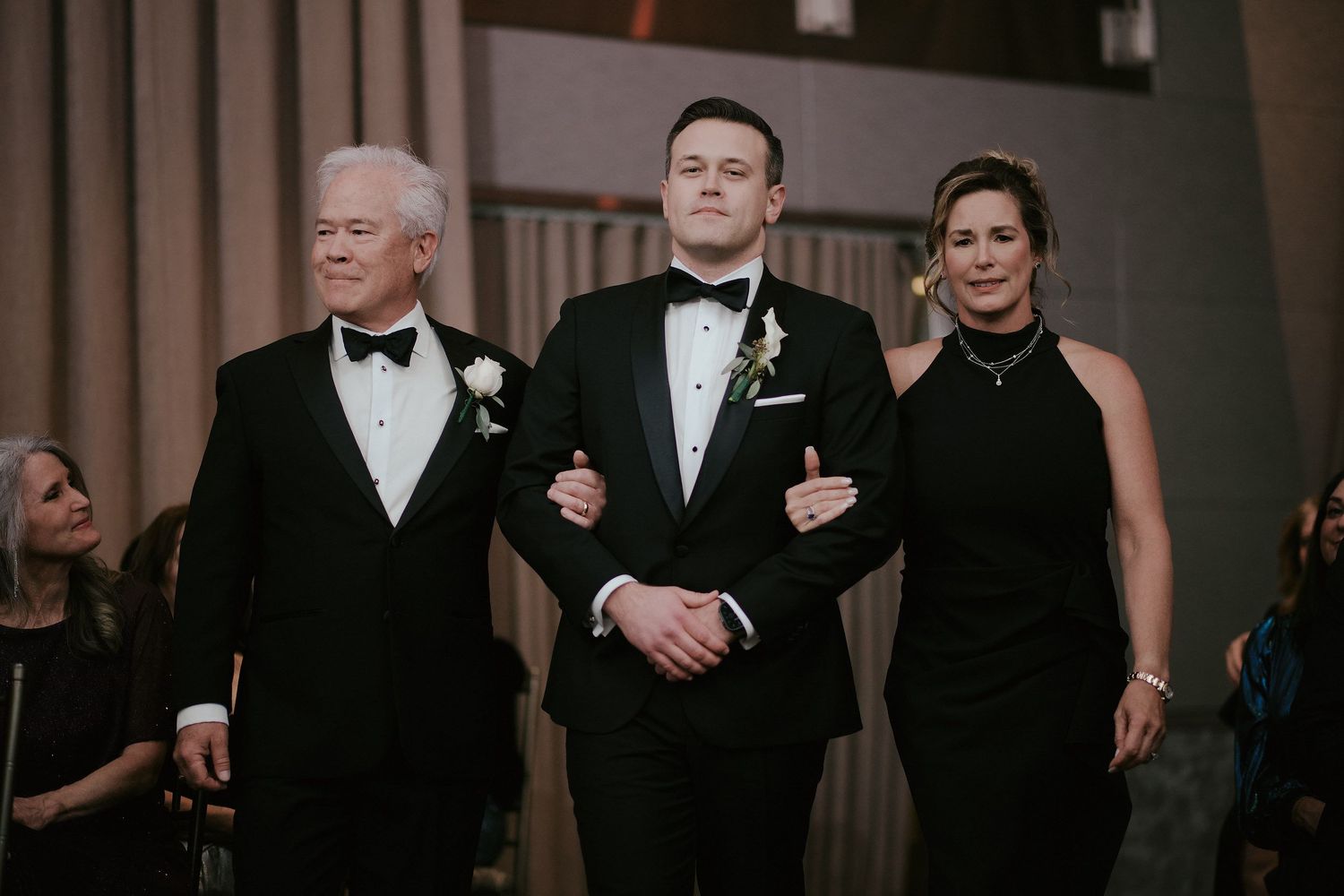 Three people dressed in formal black attire walking together at an elegant evening event.