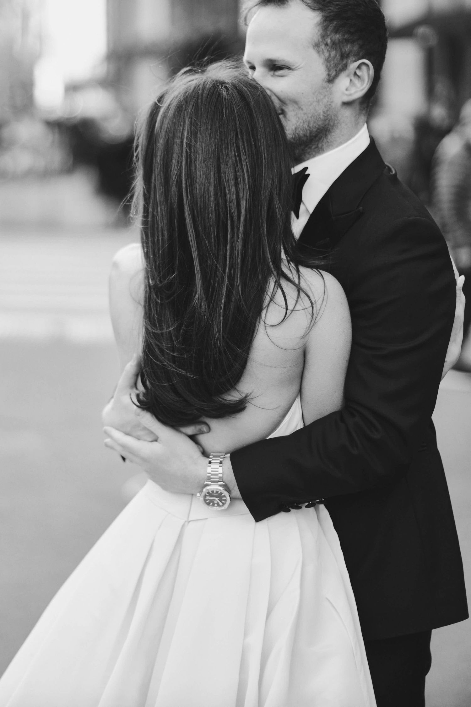 Black and white photo of a groom in a suit embracing and kissing his bride in a white wedding dress.