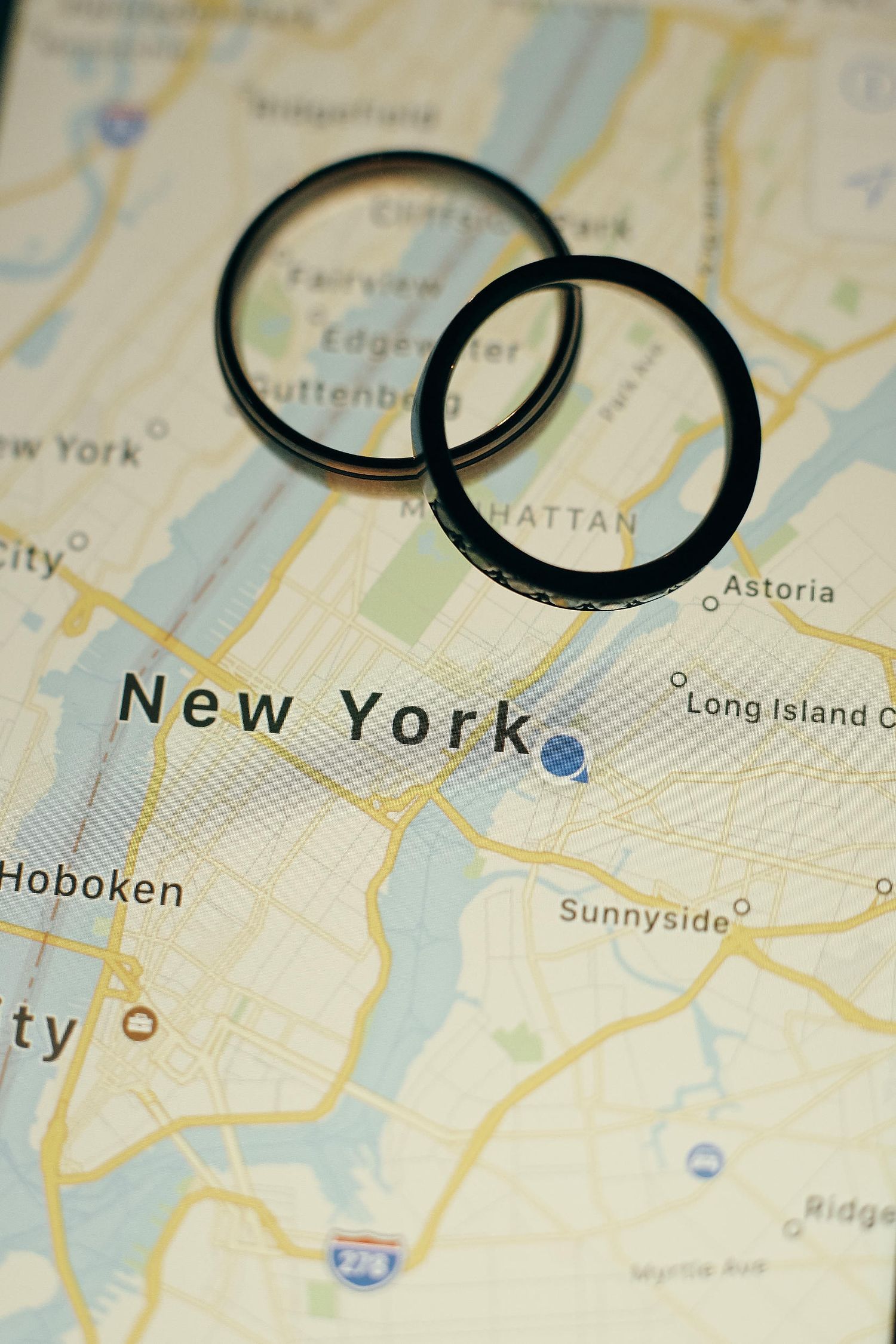 Two black wedding rings placed on a map showing New York City, Manhattan, and surrounding areas.