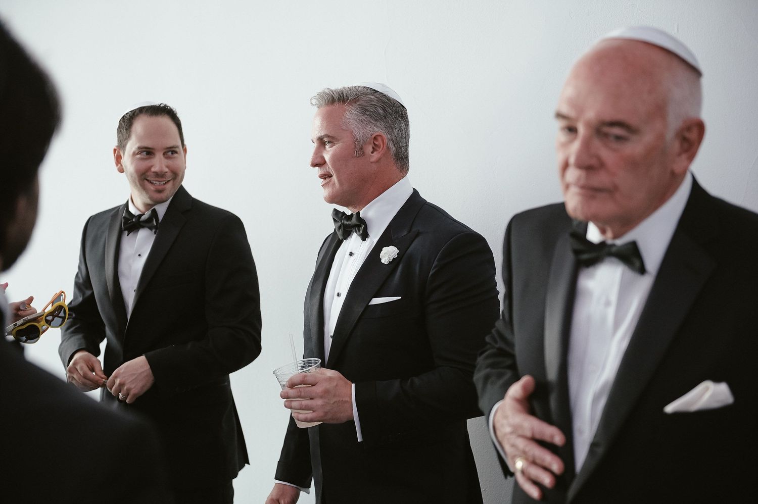 Three men in formal black tuxedos and bowties stand together at an elegant event.