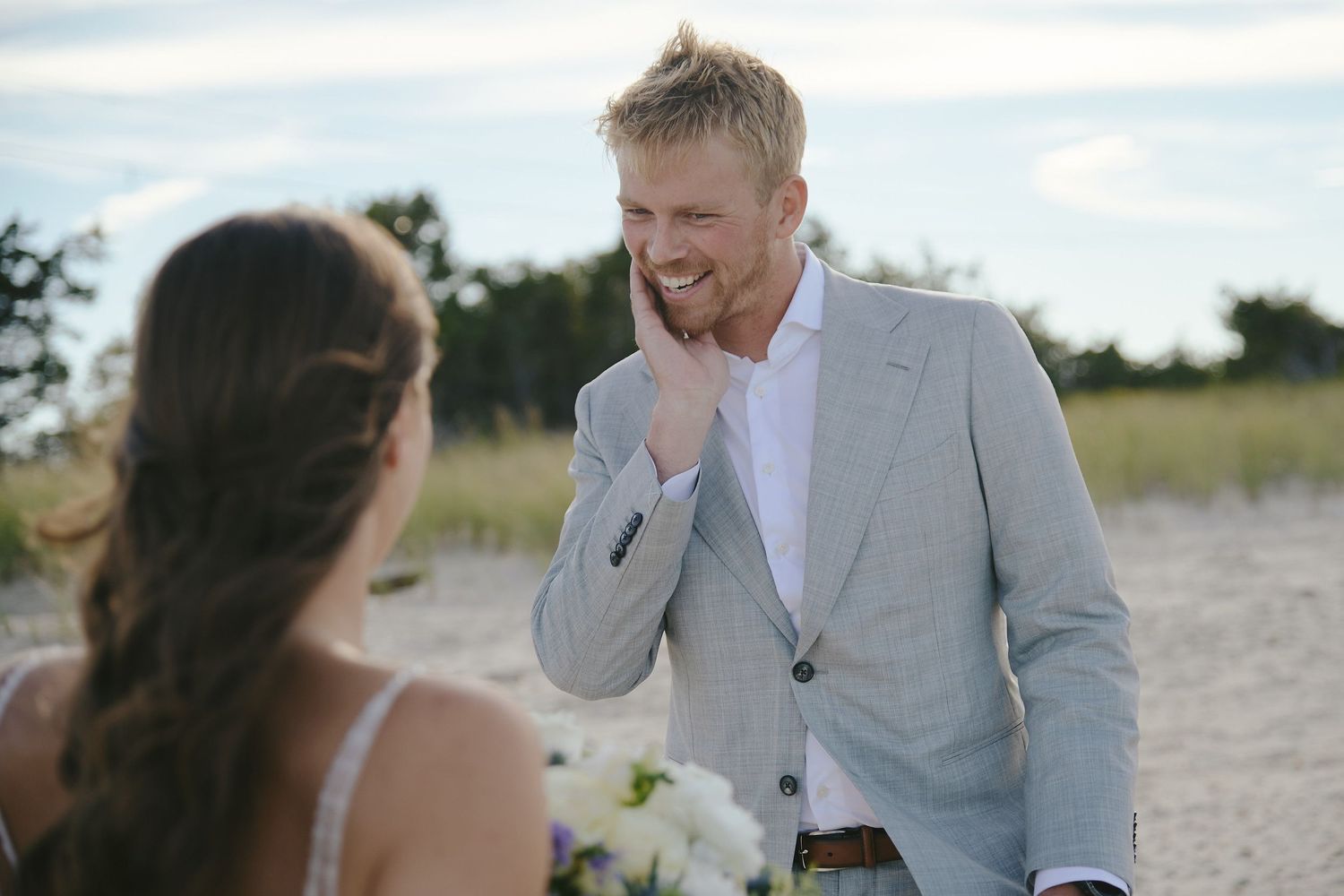 The couple shares a joyful moment together on a beach path as the groom displays a heartfelt emotional reaction.