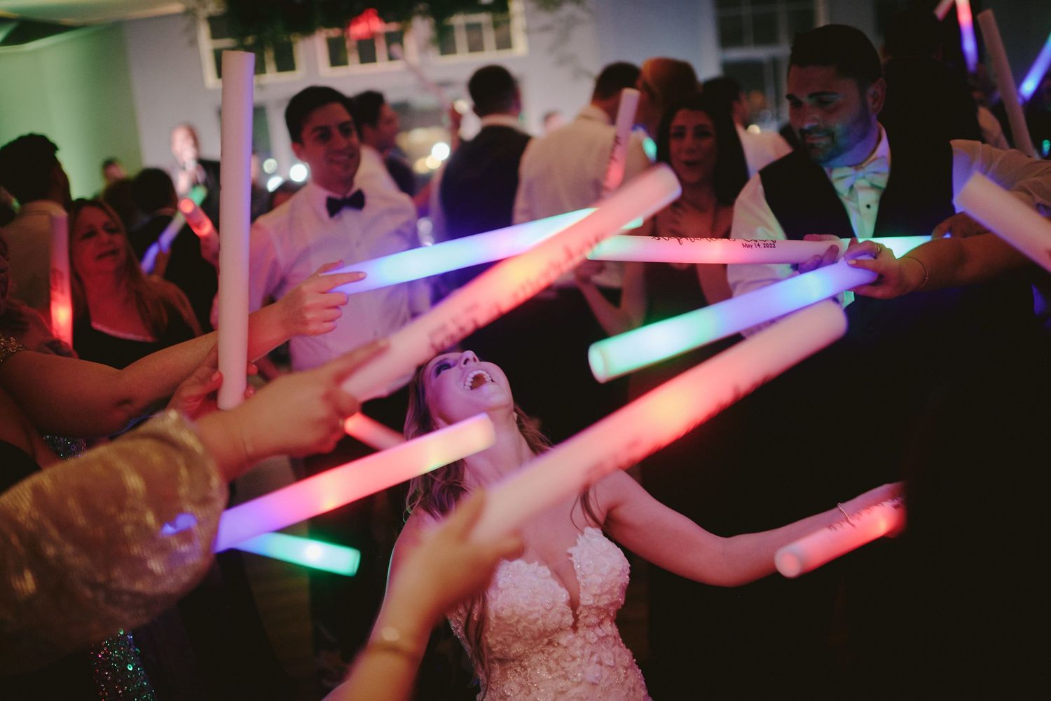 People hold colorful glowing LED light sticks while dancing at a party celebration.