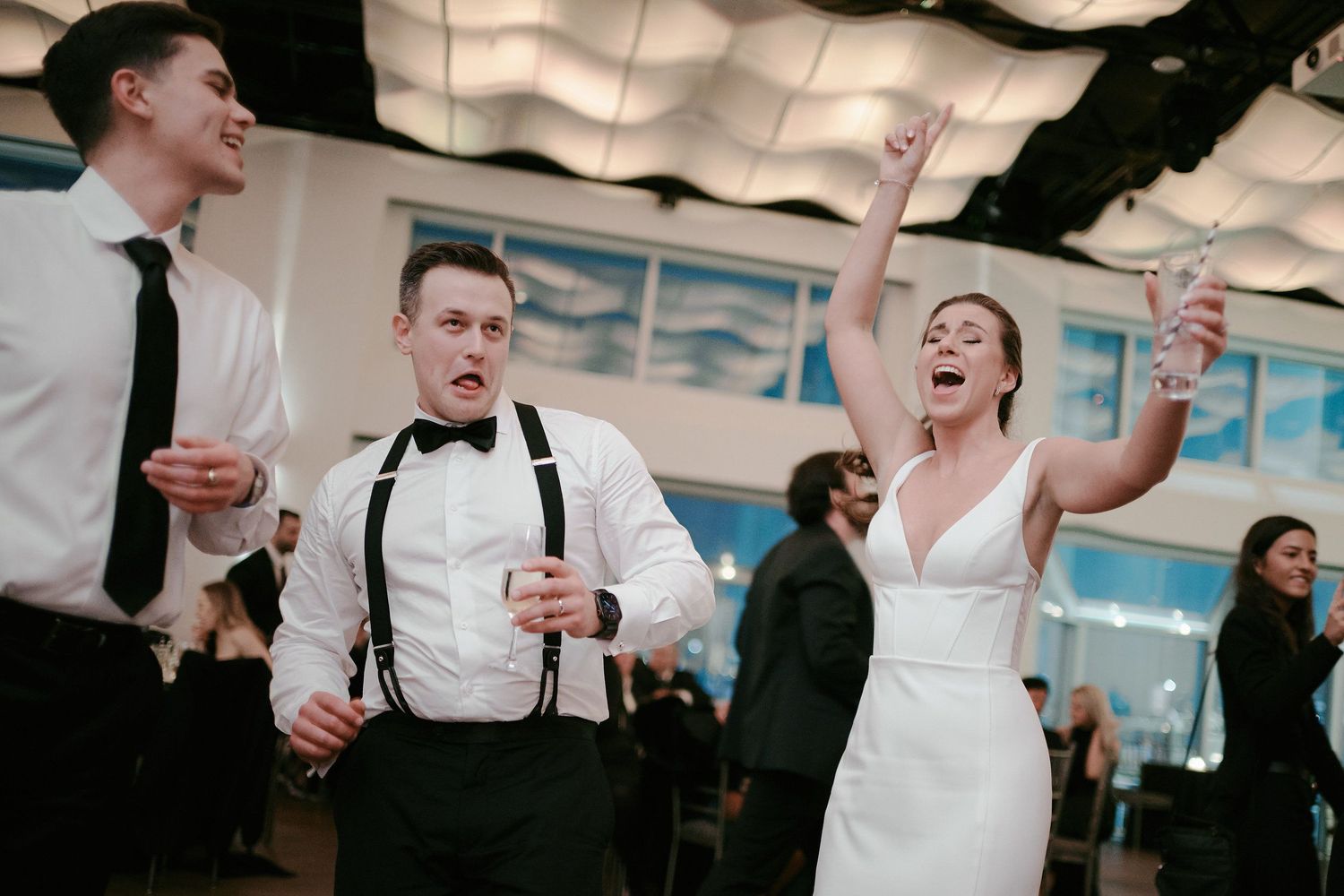 Joyful wedding celebration with people dancing and laughing during reception in bright indoor venue.