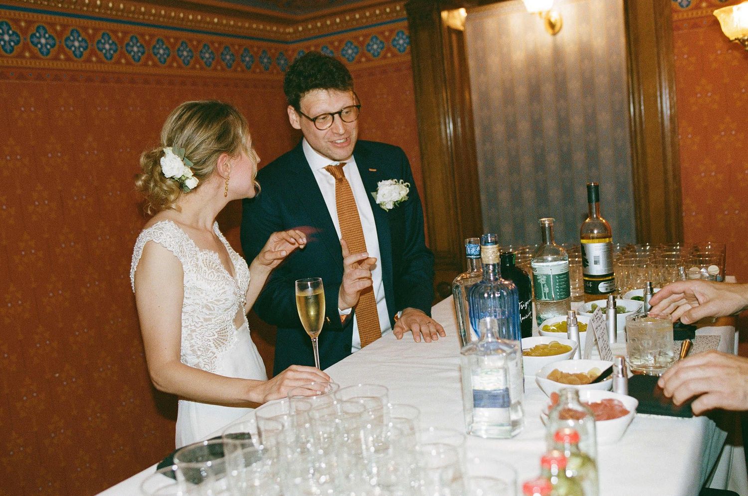 Two people sharing a moment at an elegant wedding reception bar with champagne flutes and decorative bottles.