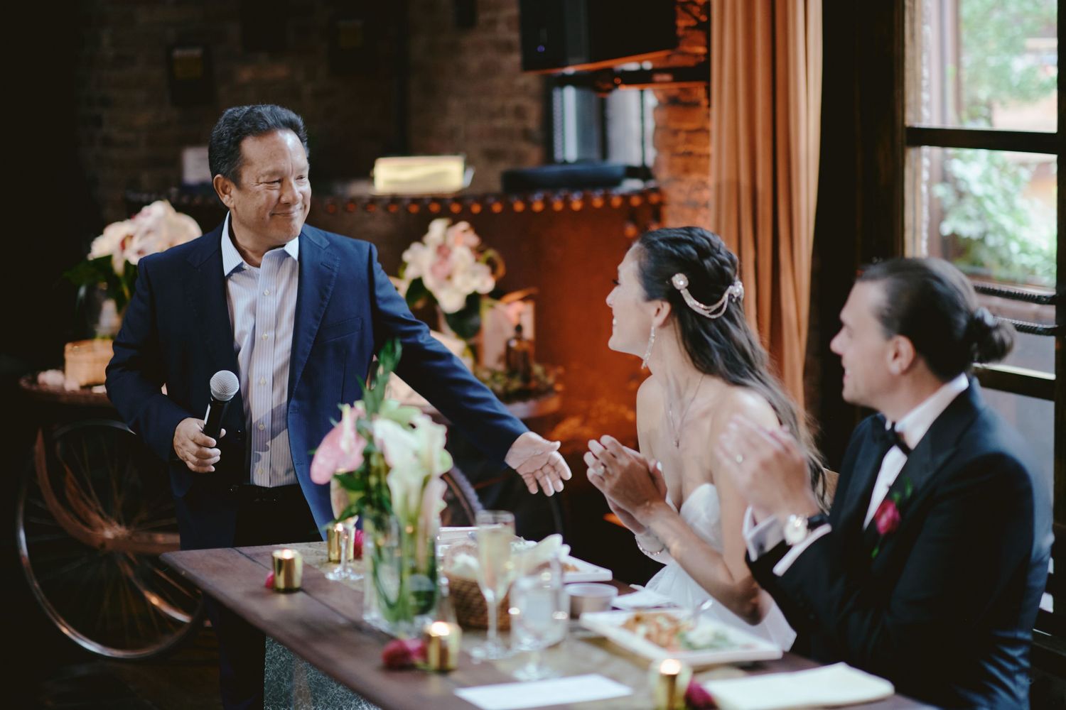 A group of people sharing a lively conversation during a celebration at a rustic indoor venue with brick walls.