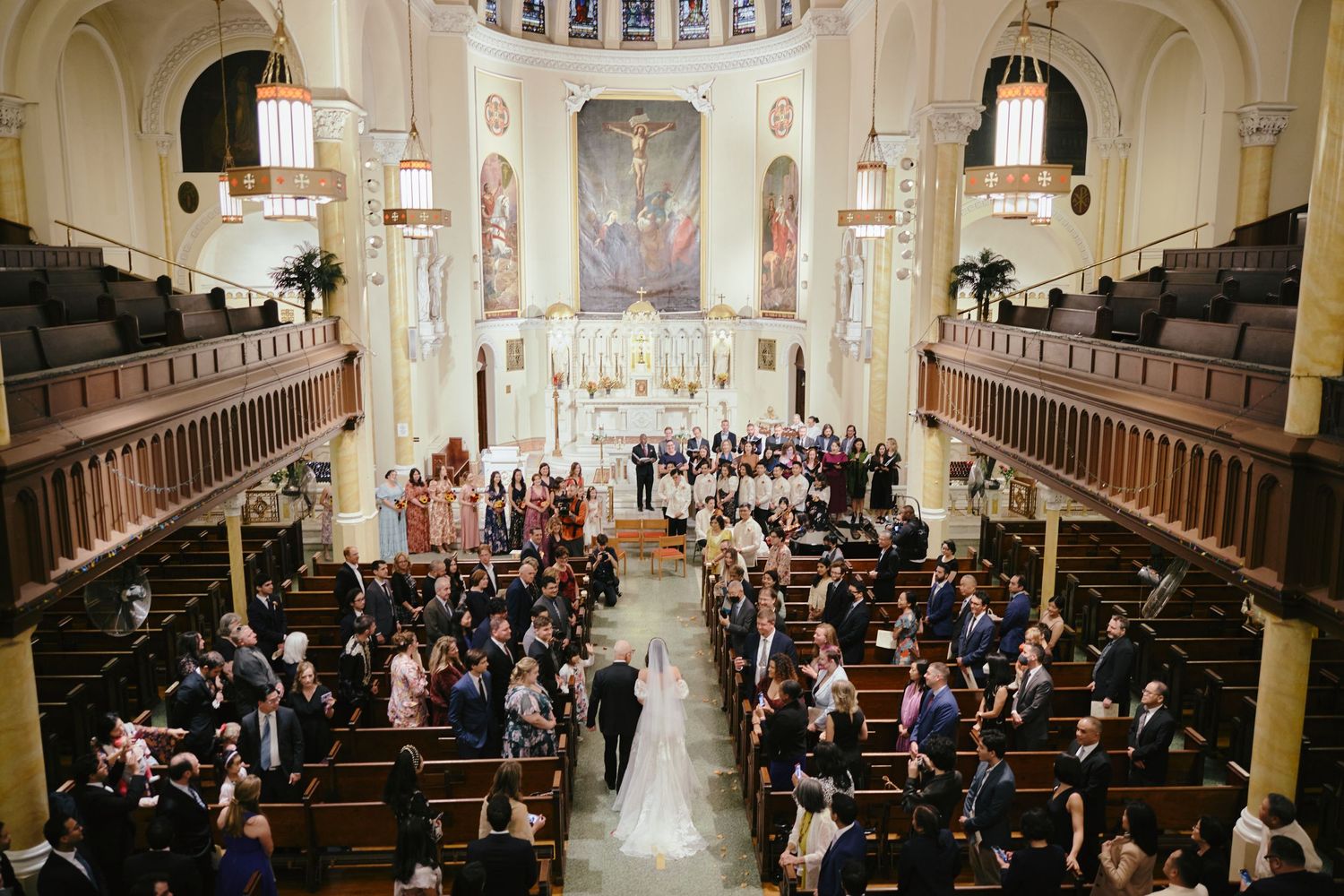 A grand church wedding ceremony viewed from above showing guests seated in wooden pews and elaborate architecture.