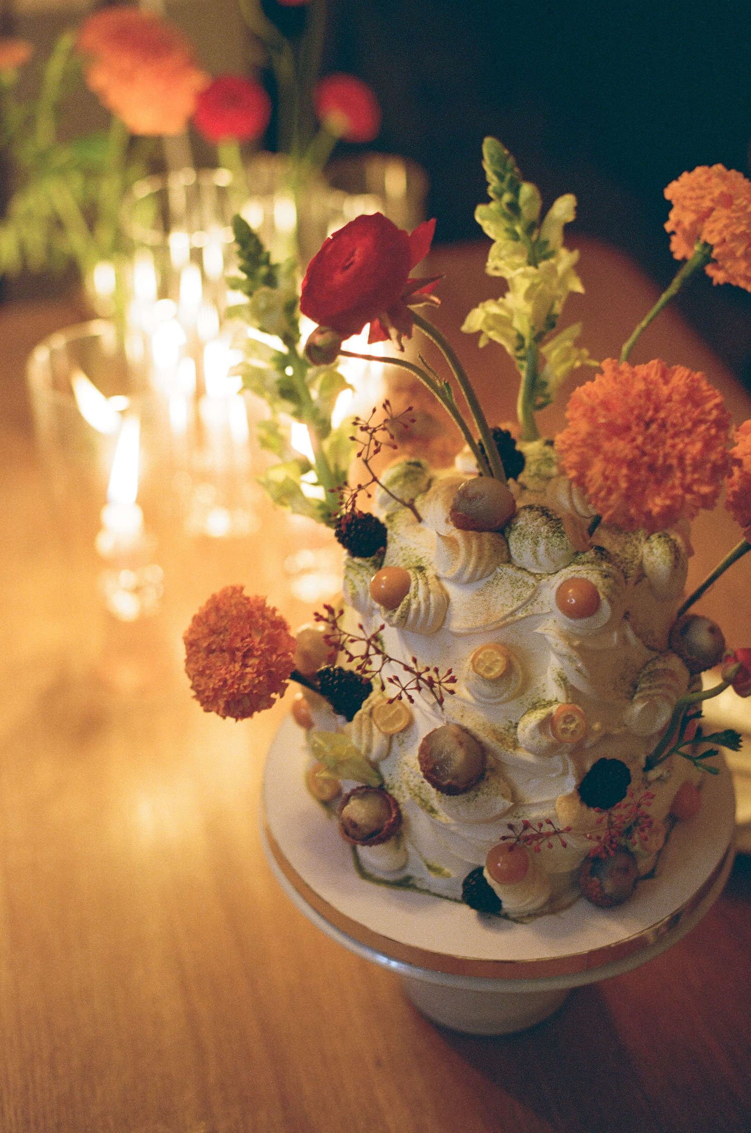 Romantic candlelit wedding cake decorated with fresh flowers, carnations and acorns in warm ambient lighting.