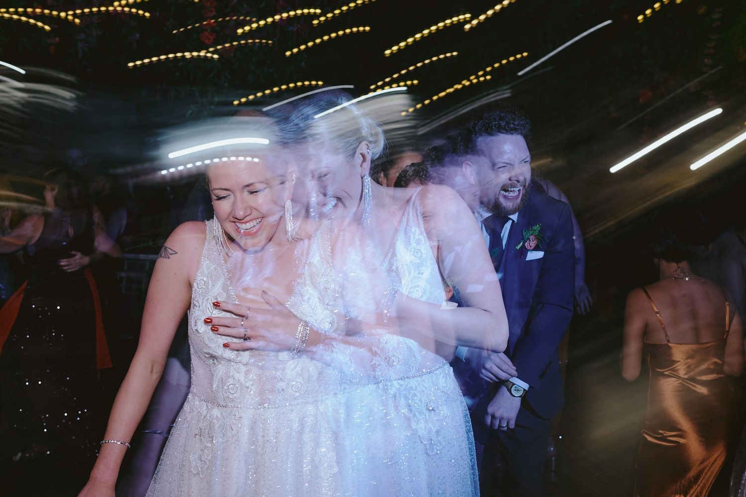 Couple dancing together at a dimly lit wedding reception with string lights overhead creating a romantic atmosphere.