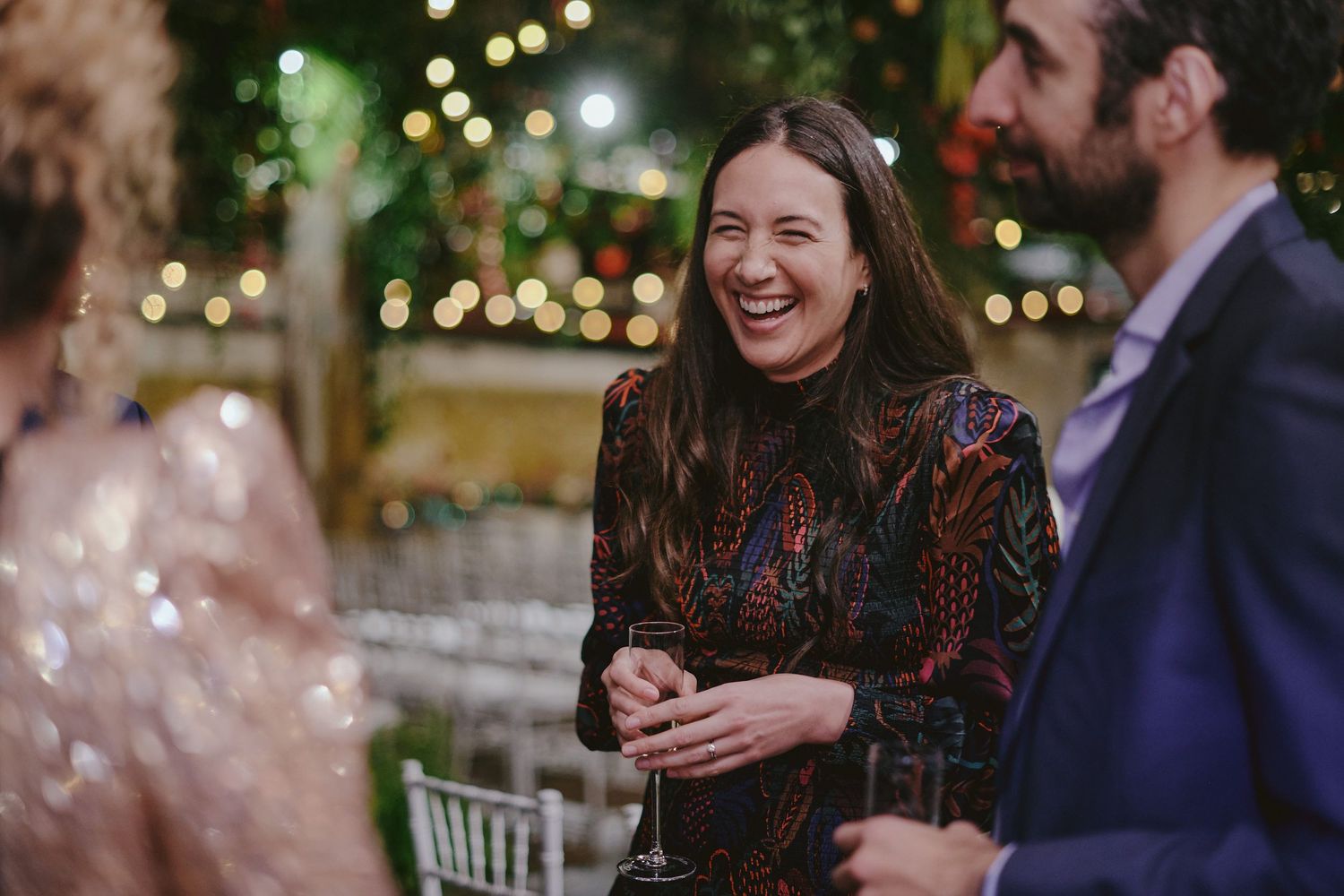 A person laughs joyfully at a social gathering with warm bokeh lighting in the background.