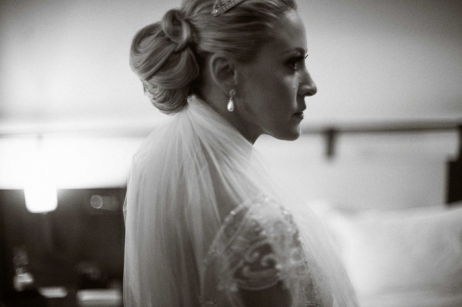 Elegant bride in white turtleneck lace gown shows profile view with hair in classic updo style in black and white shot.