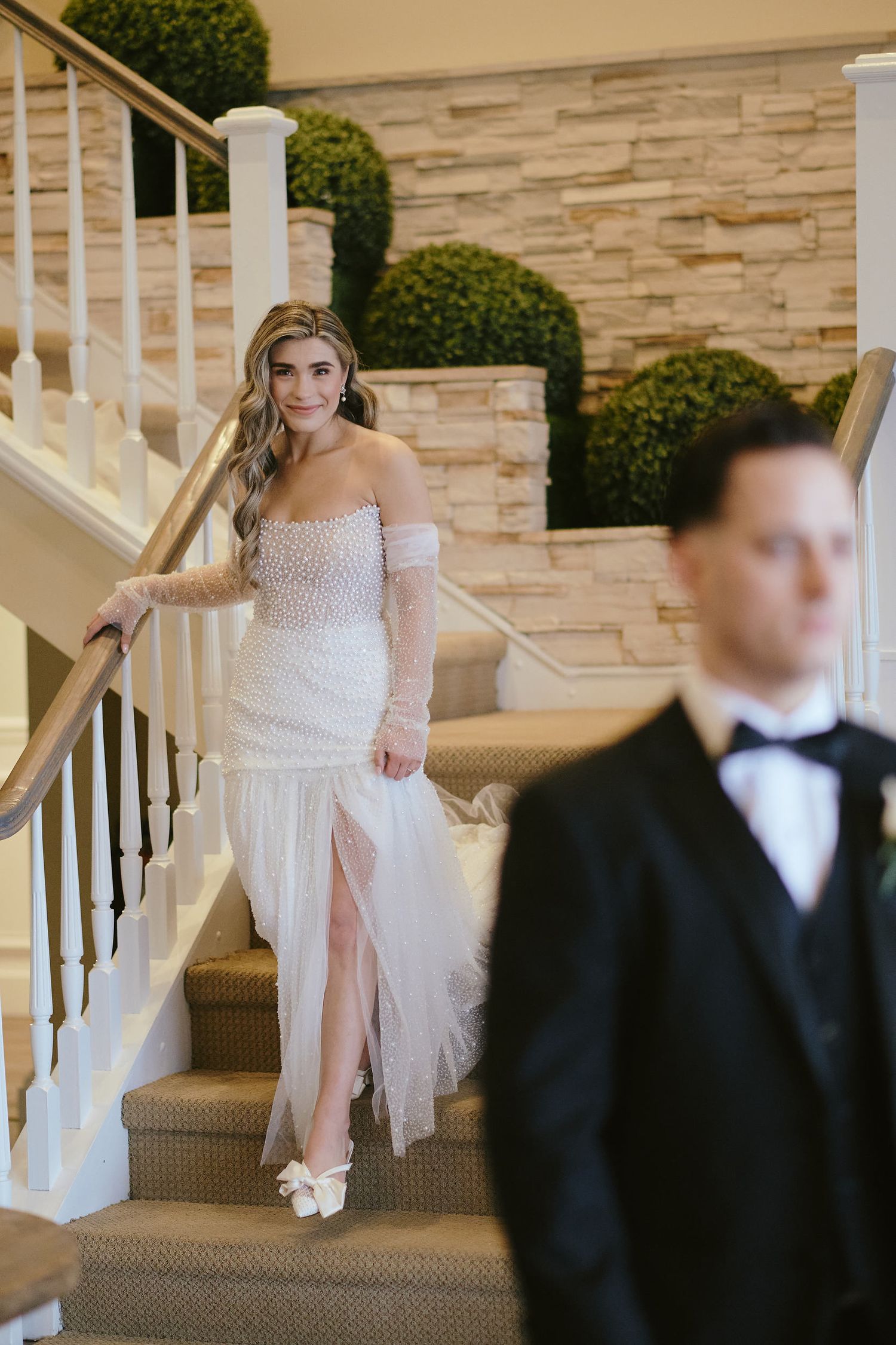 Elegant wedding couple during their first look moment on carpeted stairs with stone wall backdrop.