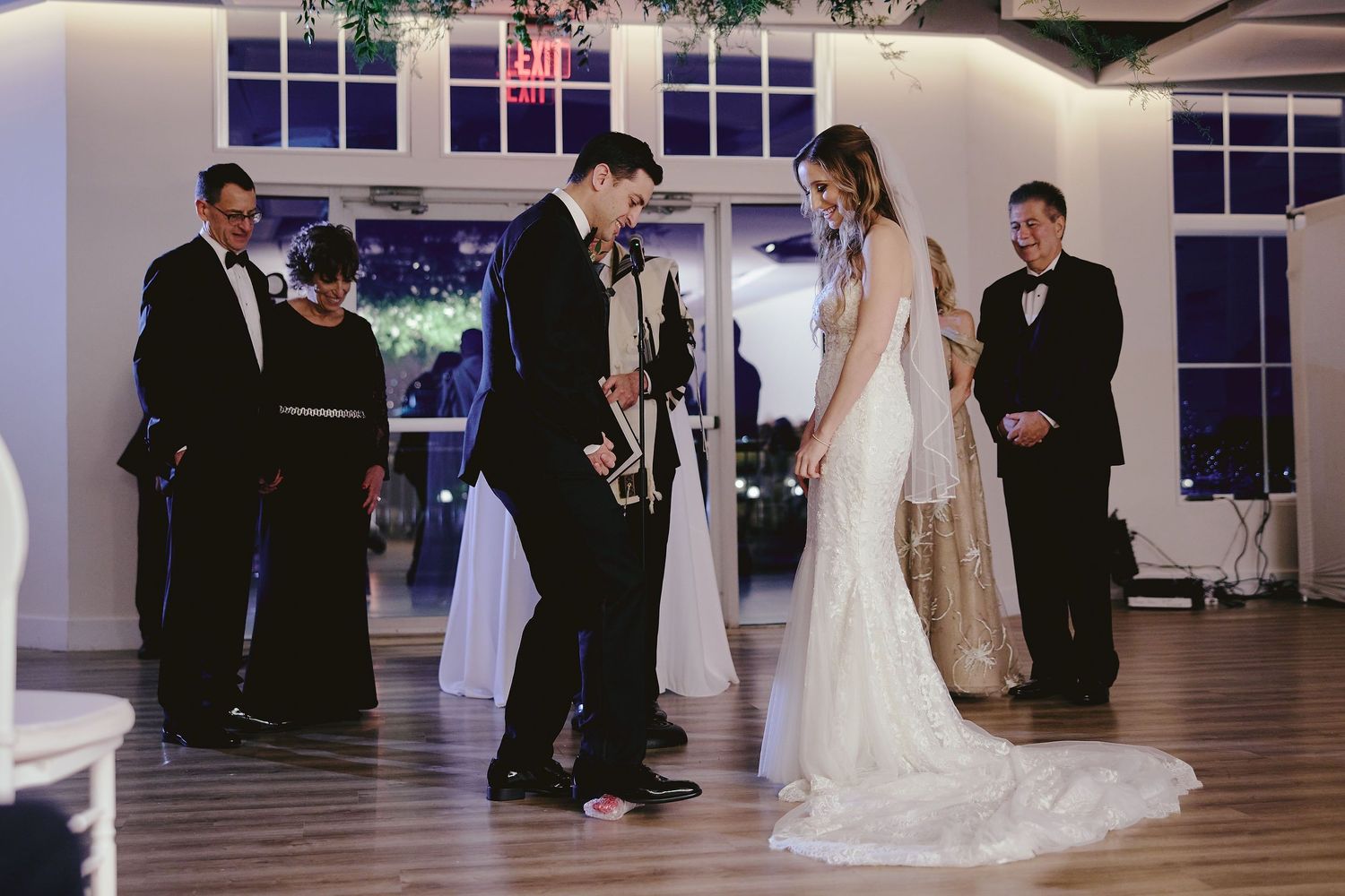 Couple sharing their first dance at evening wedding reception with guests and string lights in elegant venue.