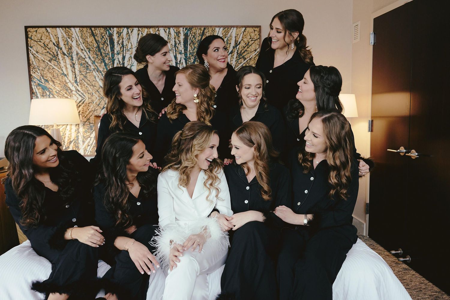 A group wearing coordinated black outfits gathers around a person in white for a candid indoor celebratory moment.