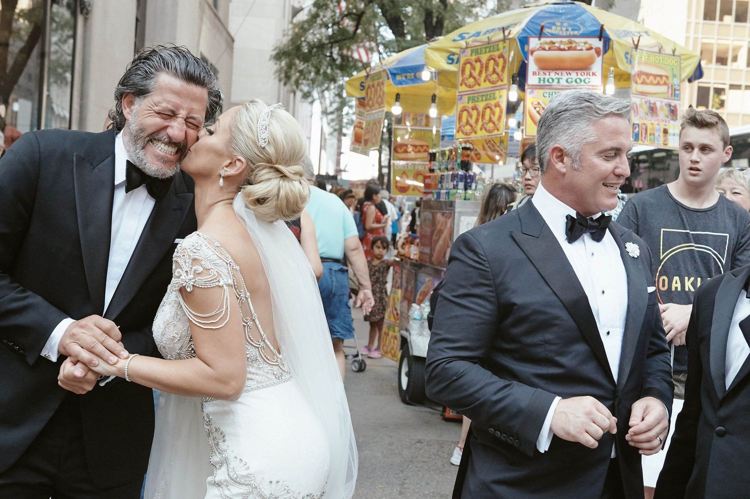 People in formal attire including someone in a white wedding dress enjoying time together at a festive outdoor event.