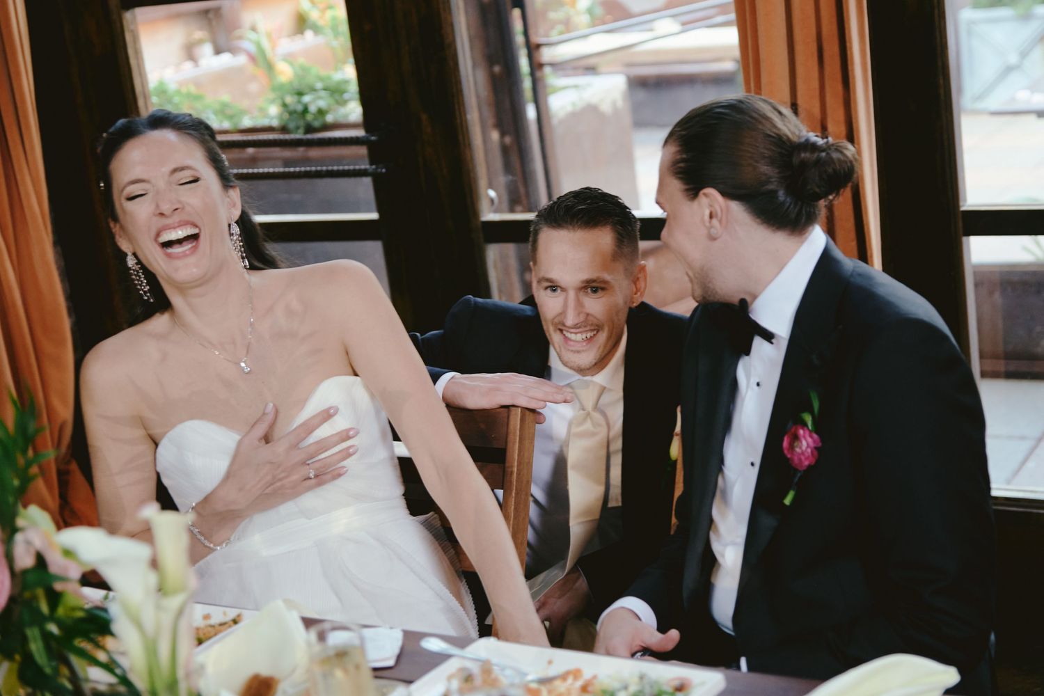 Joyful wedding moment captured during reception as guests share a candid laugh at dining table.