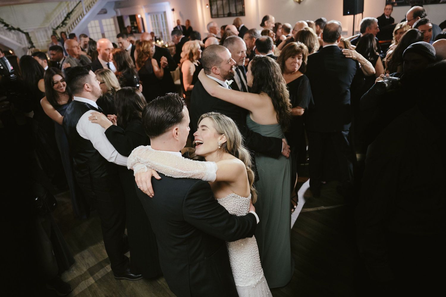 A couple dances closely together surrounded by other guests on a crowded wedding reception dance floor.