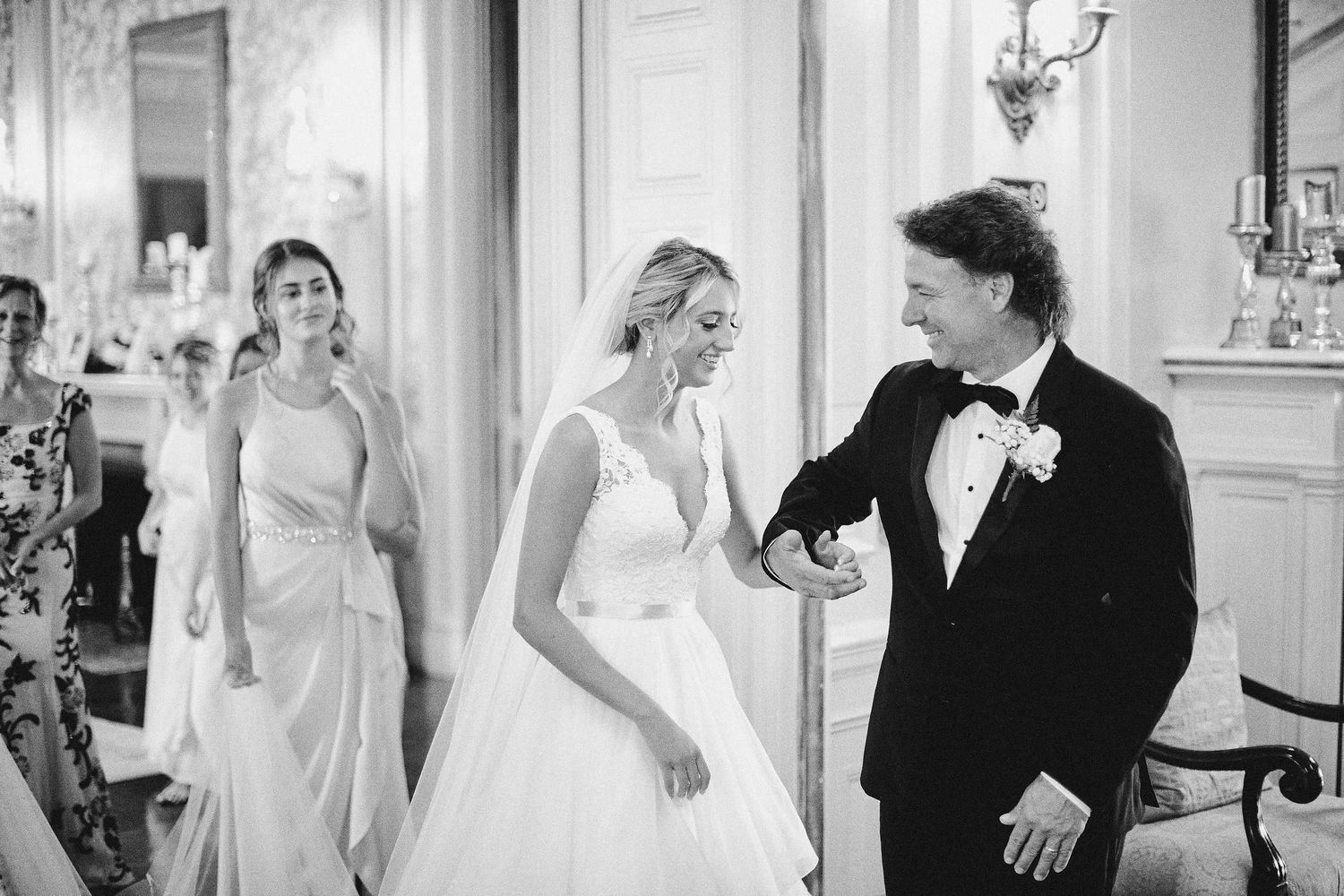 A black and white candid moment at an elegant wedding reception with people in formal attire interacting in a grand venue.