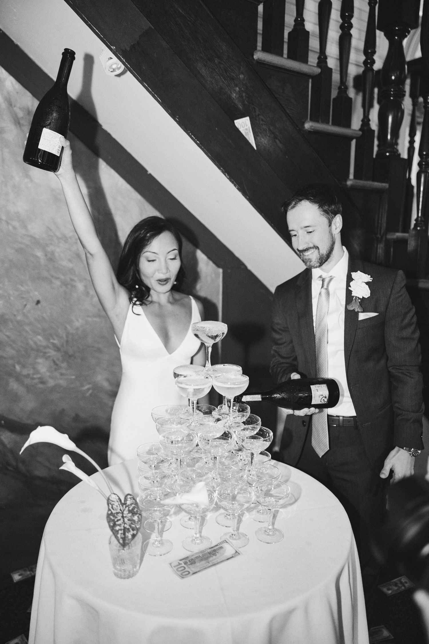 Bride and groom pouring champagne tower at wedding reception in black and white photo.