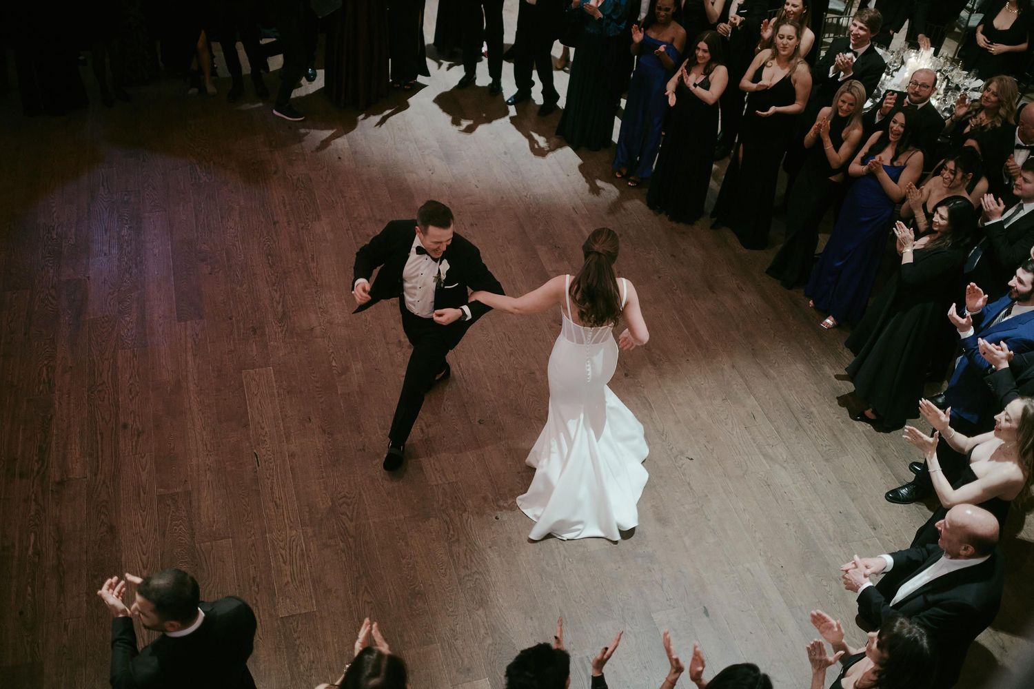 Beautiful first dance at a wedding with guests watching from the sides of a polished wooden dance floor.