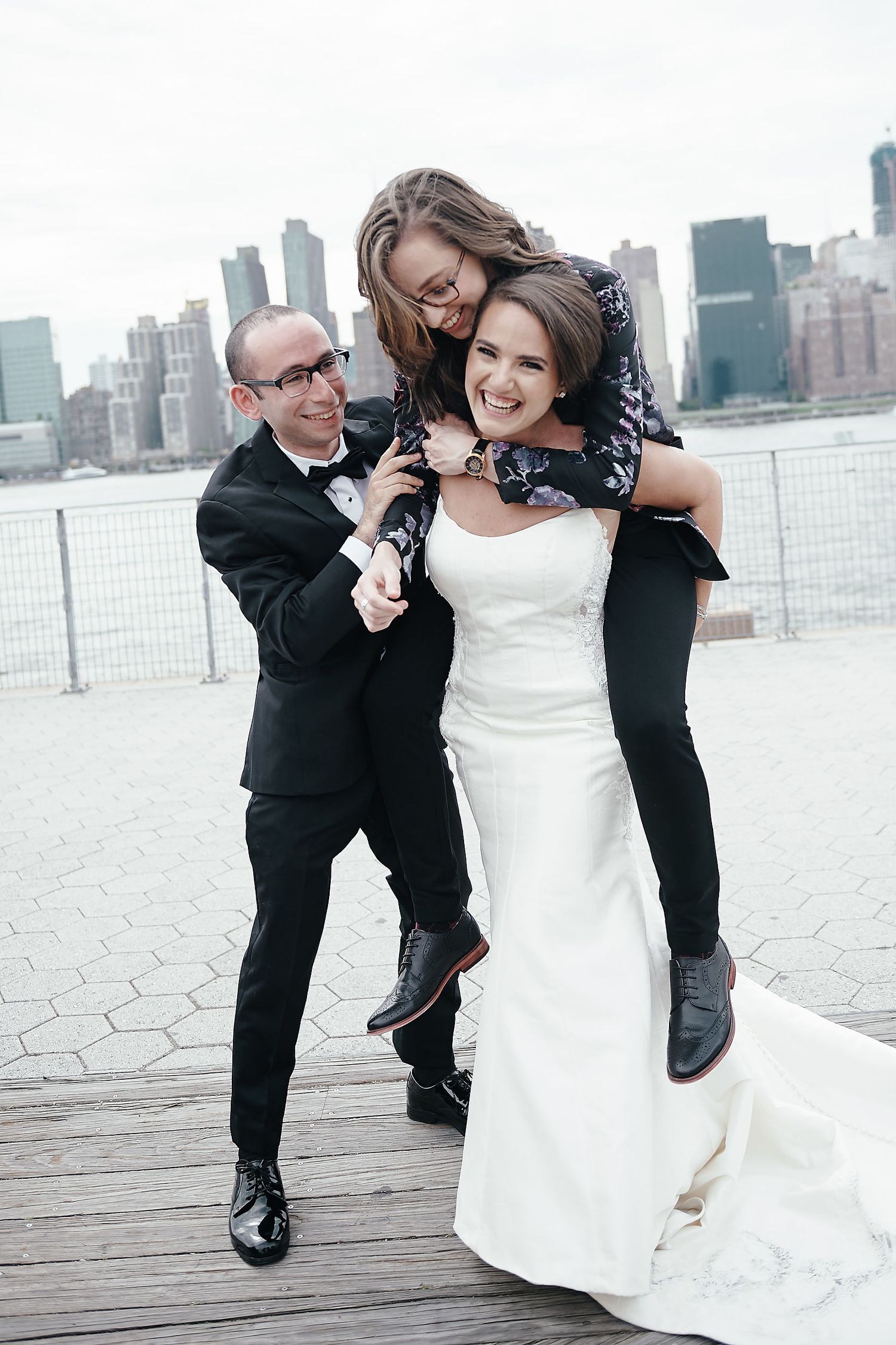 A playful wedding party moment on a waterfront boardwalk with the city skyline in the background.