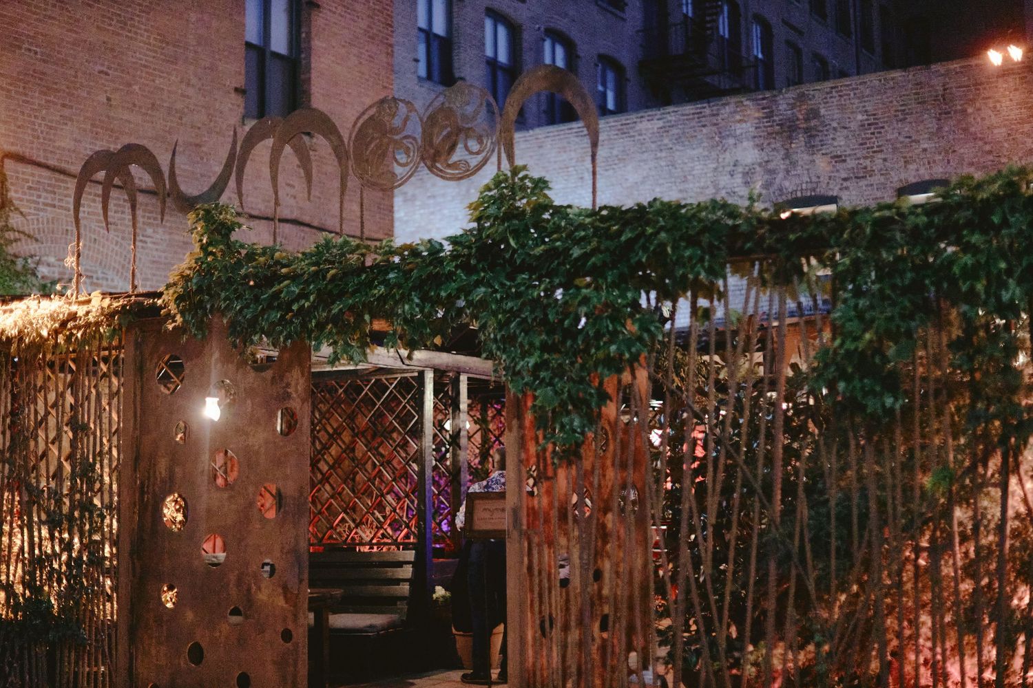 A rustic outdoor garden patio decorated with fairy lights and wooden lattice fencing covered in climbing ivy vines.