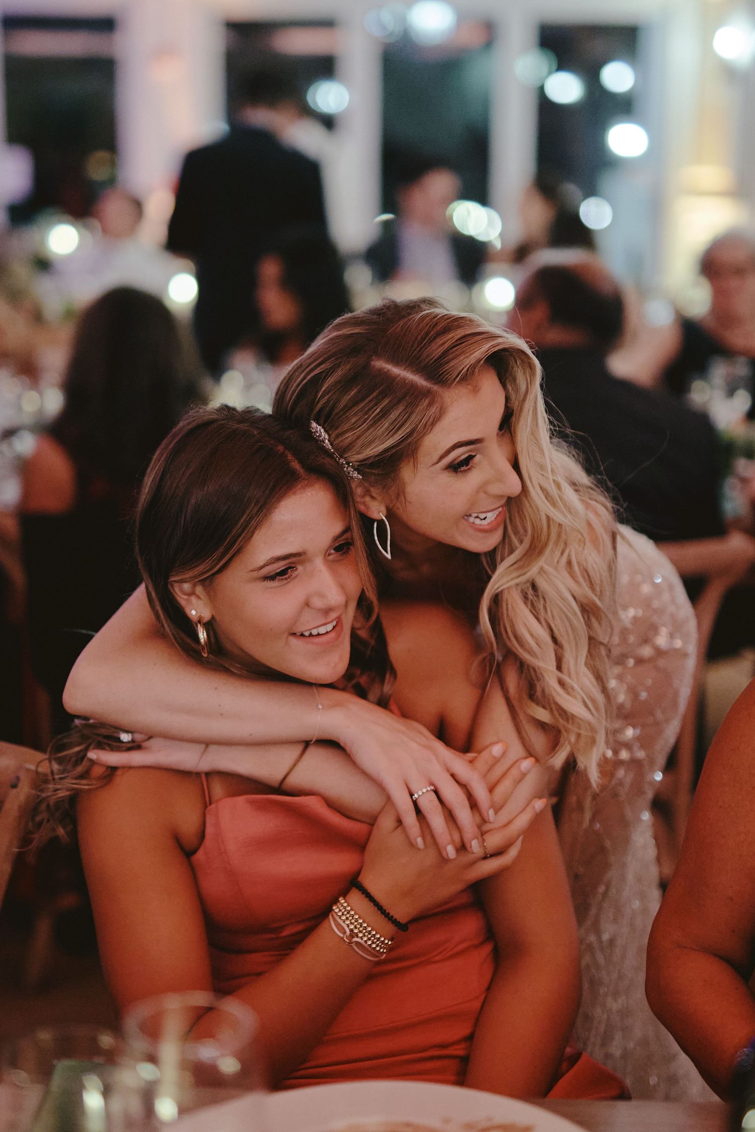 Two friends sharing a joyful moment at an evening event with a warm ambiance and bokeh lights in the background.
