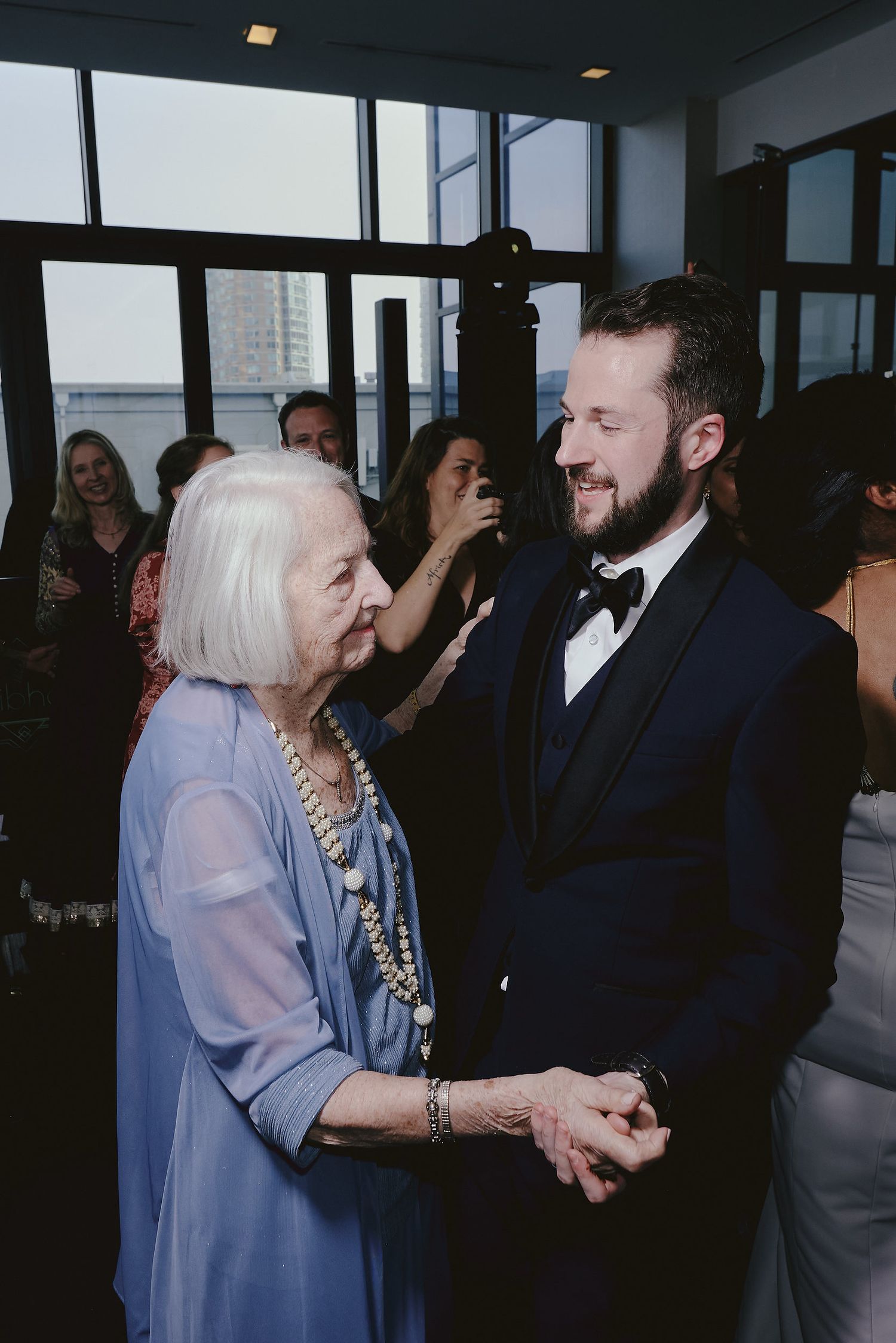 Elegant formal event moment shows older woman in blue dress and person in black tuxedo sharing a joyful conversation.