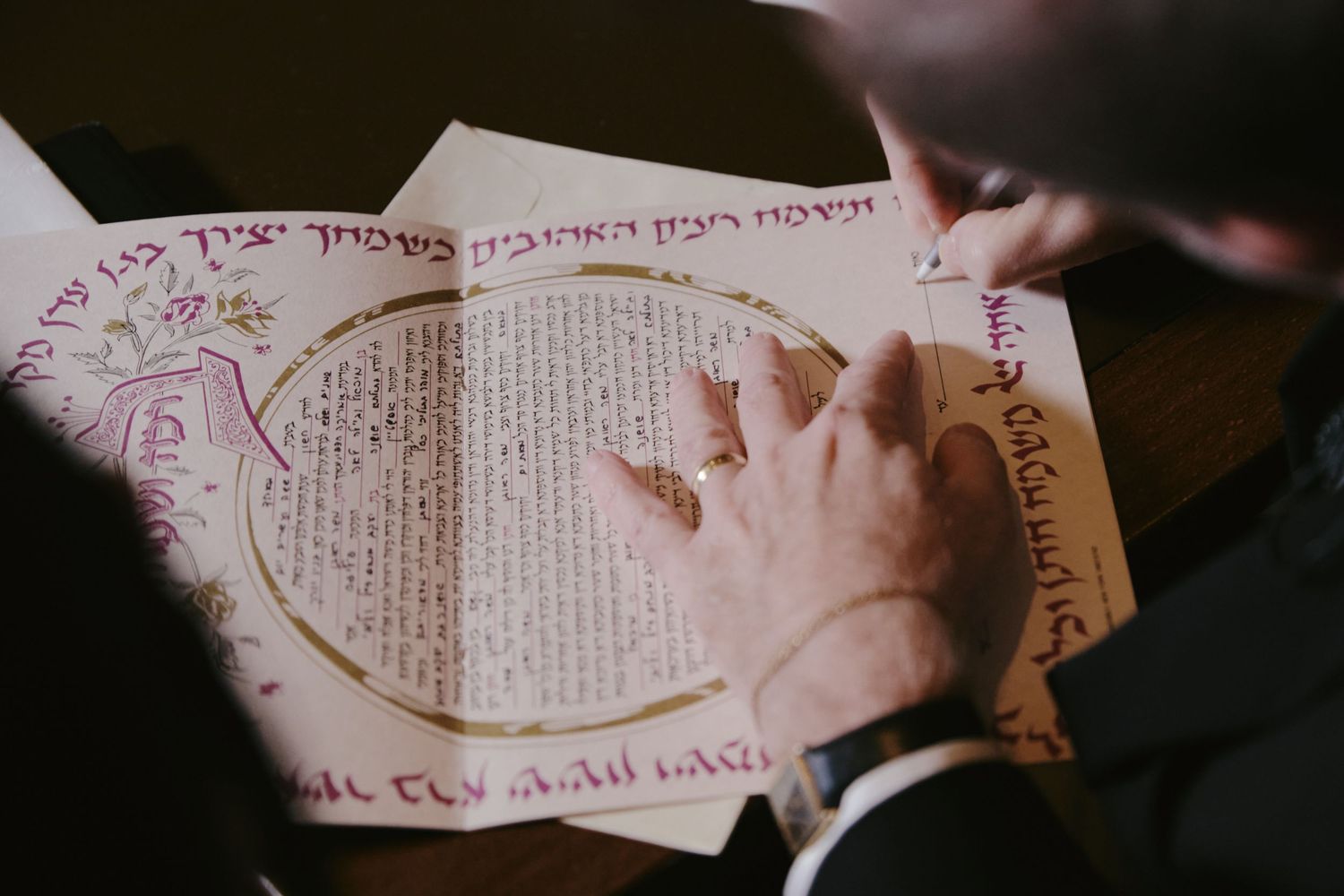 A hand rests on an open ancient manuscript with circular Hebrew text and calligraphy visible on its pages.