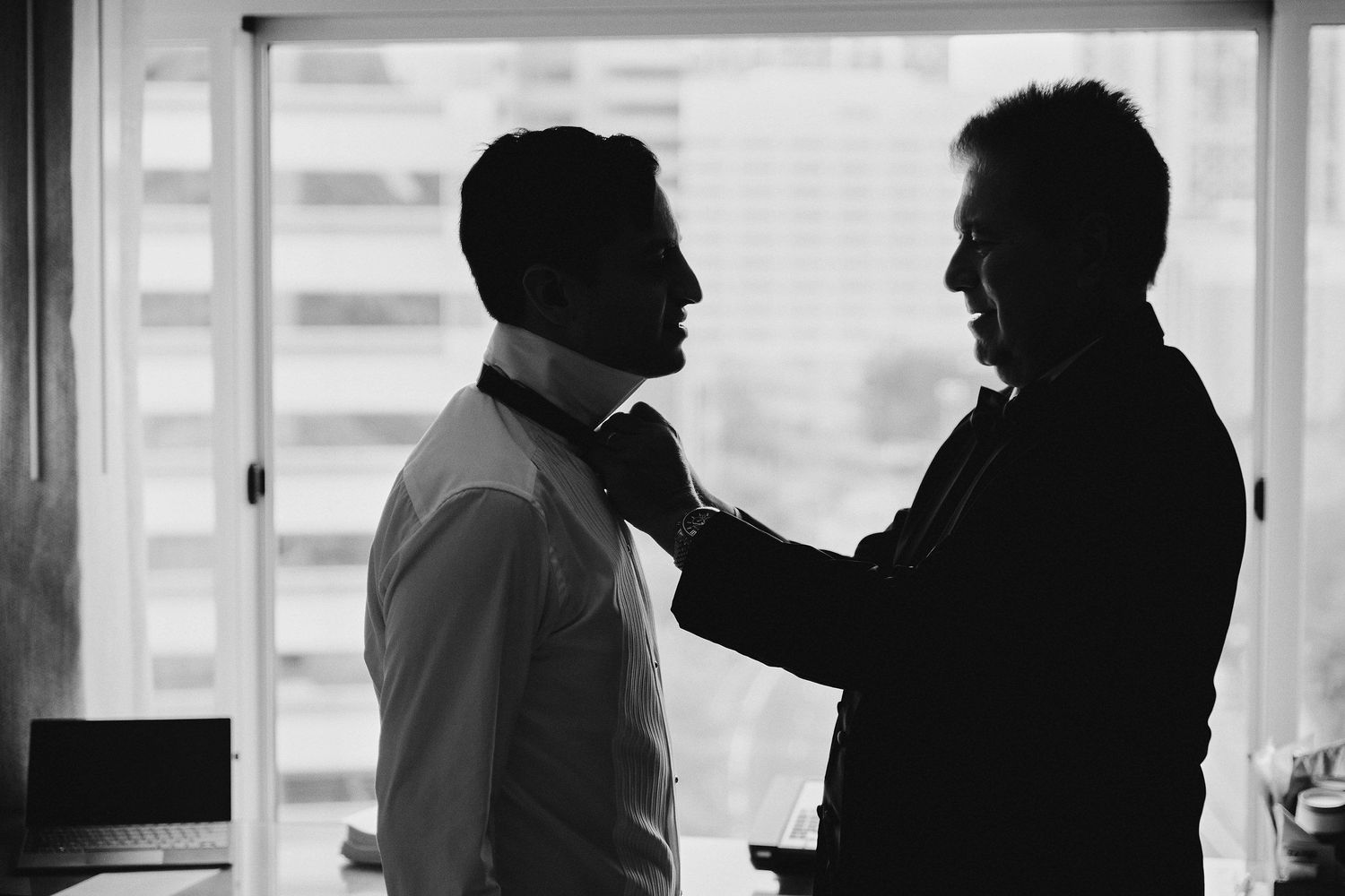 Two silhouettes engaged in intimate conversation by a window in dramatic black and white lighting.