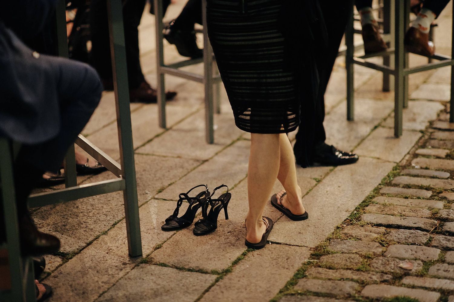 Discarded high heels sit on a cobblestone path next to formal attire at an evening event.
