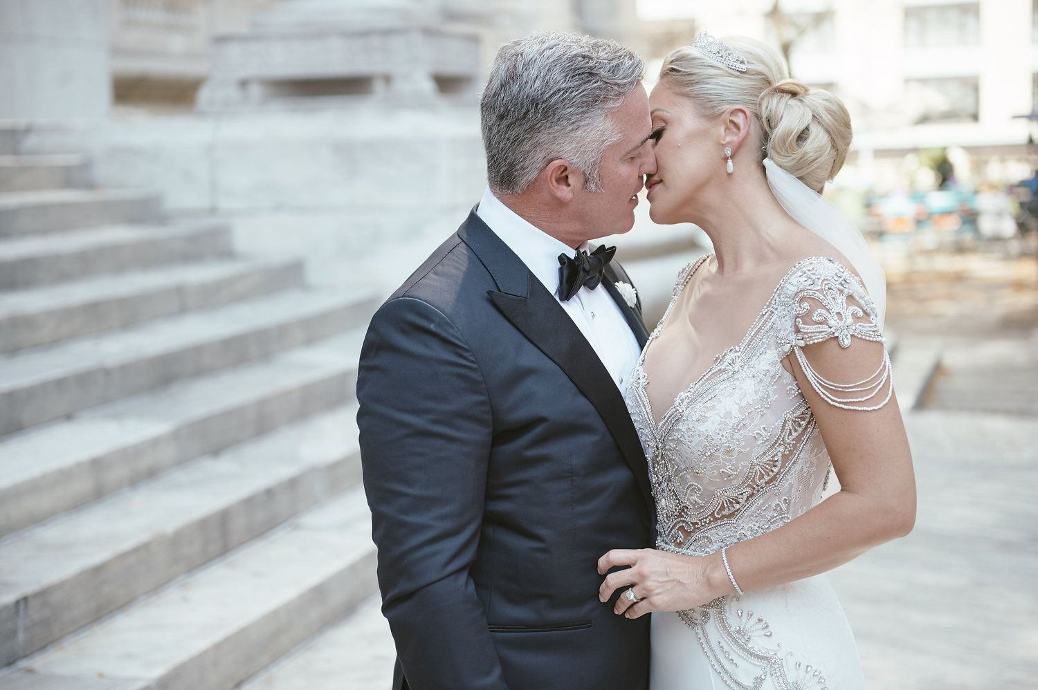 A tender wedding kiss on stone steps with the bride in a beaded gown and groom in classic black tuxedo.